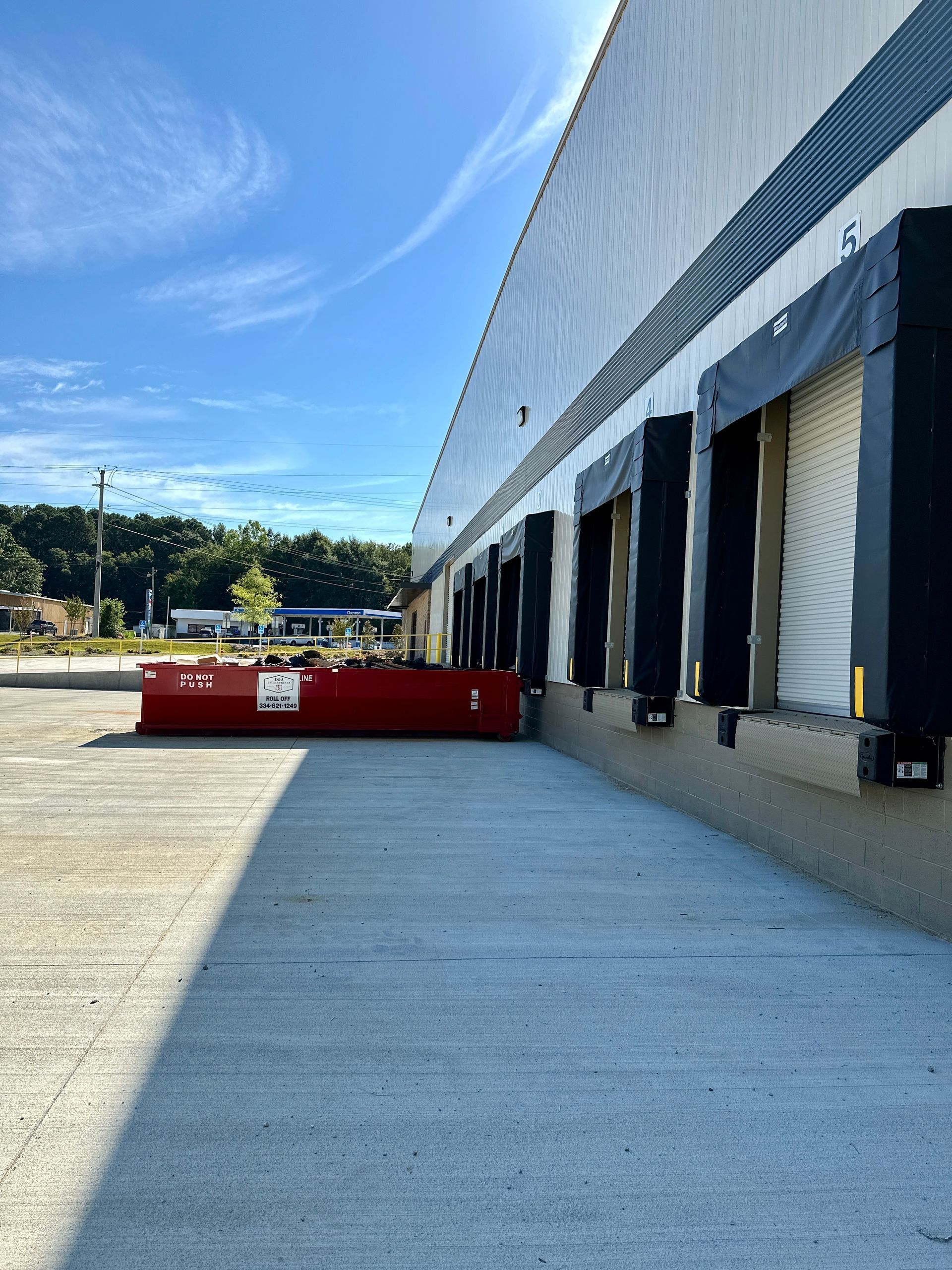 A warehouse with a lot of loading docks and a red dumpster in front of it.
