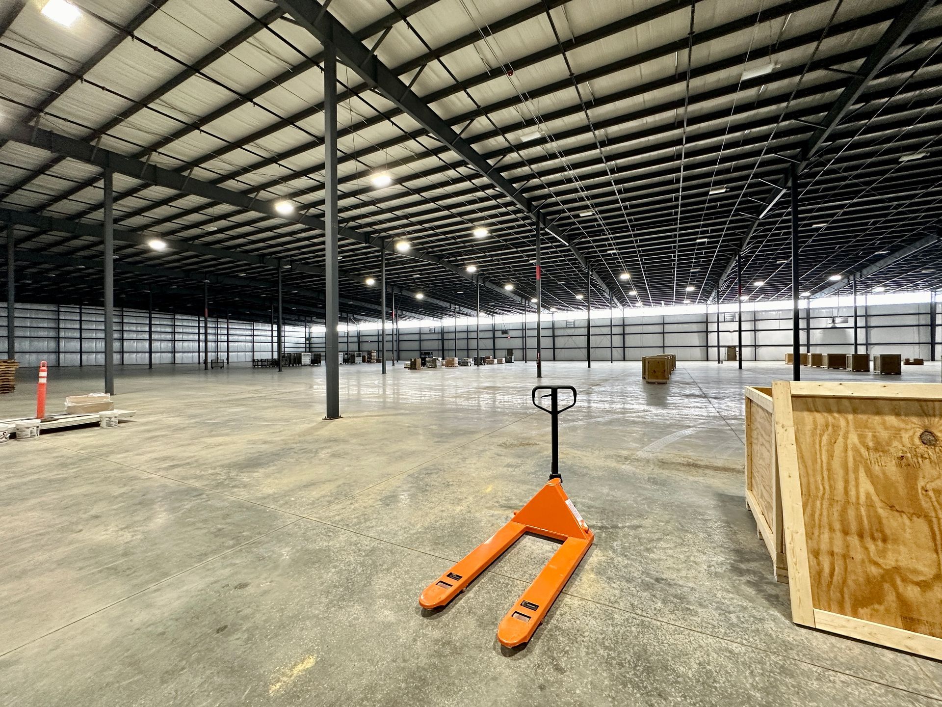 An orange hand truck is sitting in the middle of an empty warehouse.