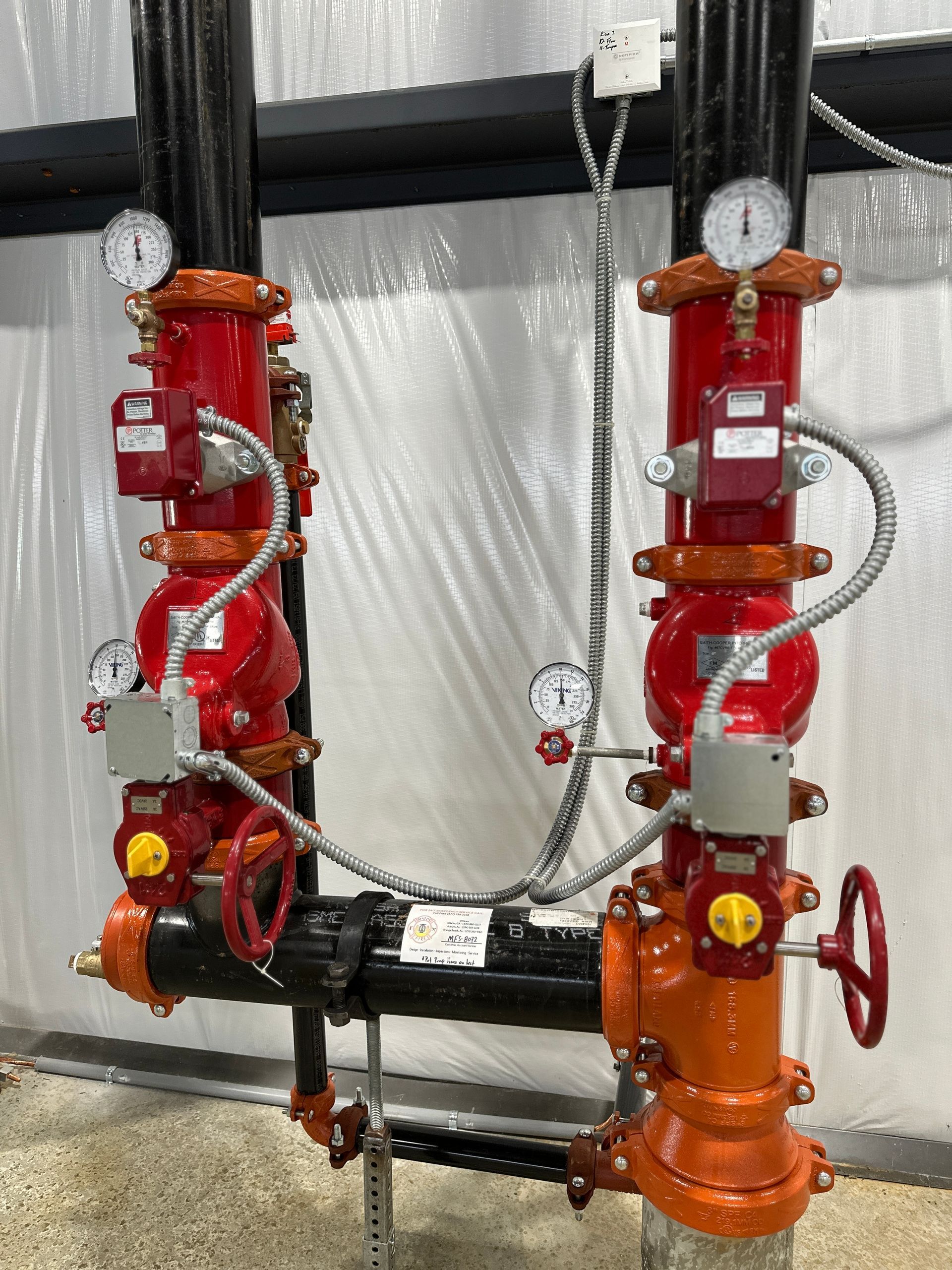 A couple of red pipes with gauges attached to them are sitting next to each other in a room.