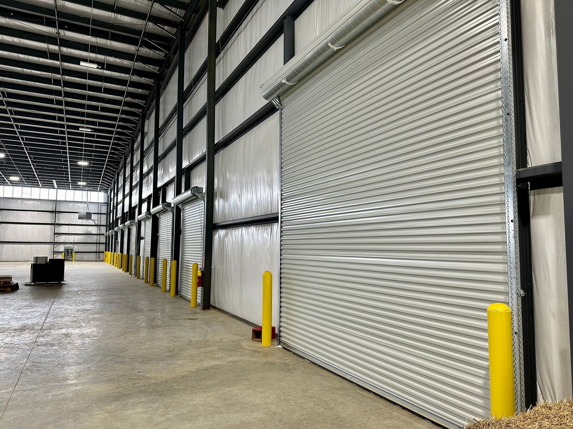 A large warehouse with a lot of rolling doors and yellow poles.