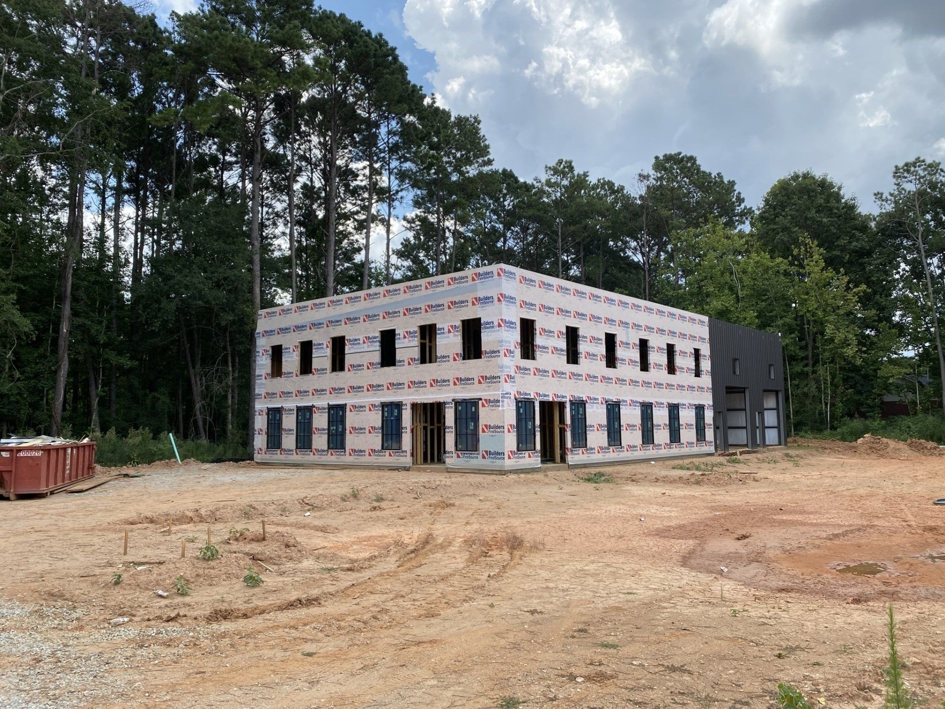 A large building is being built in the middle of a dirt field surrounded by trees.