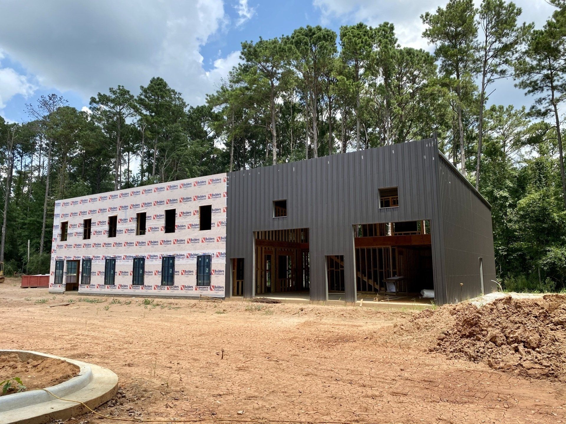 A large building is being built in the middle of a dirt field surrounded by trees.
