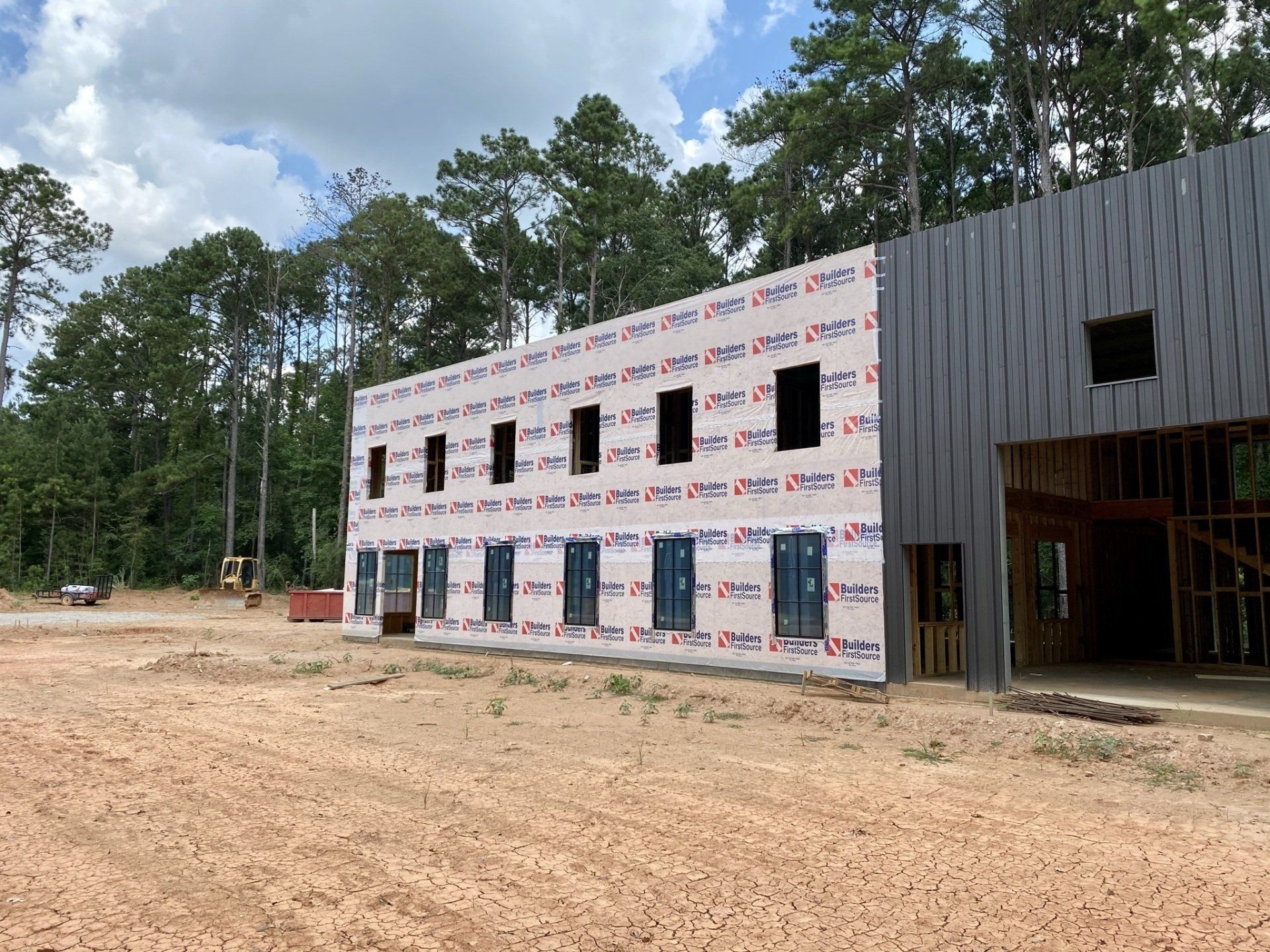 A large building is being built in a field with trees in the background.