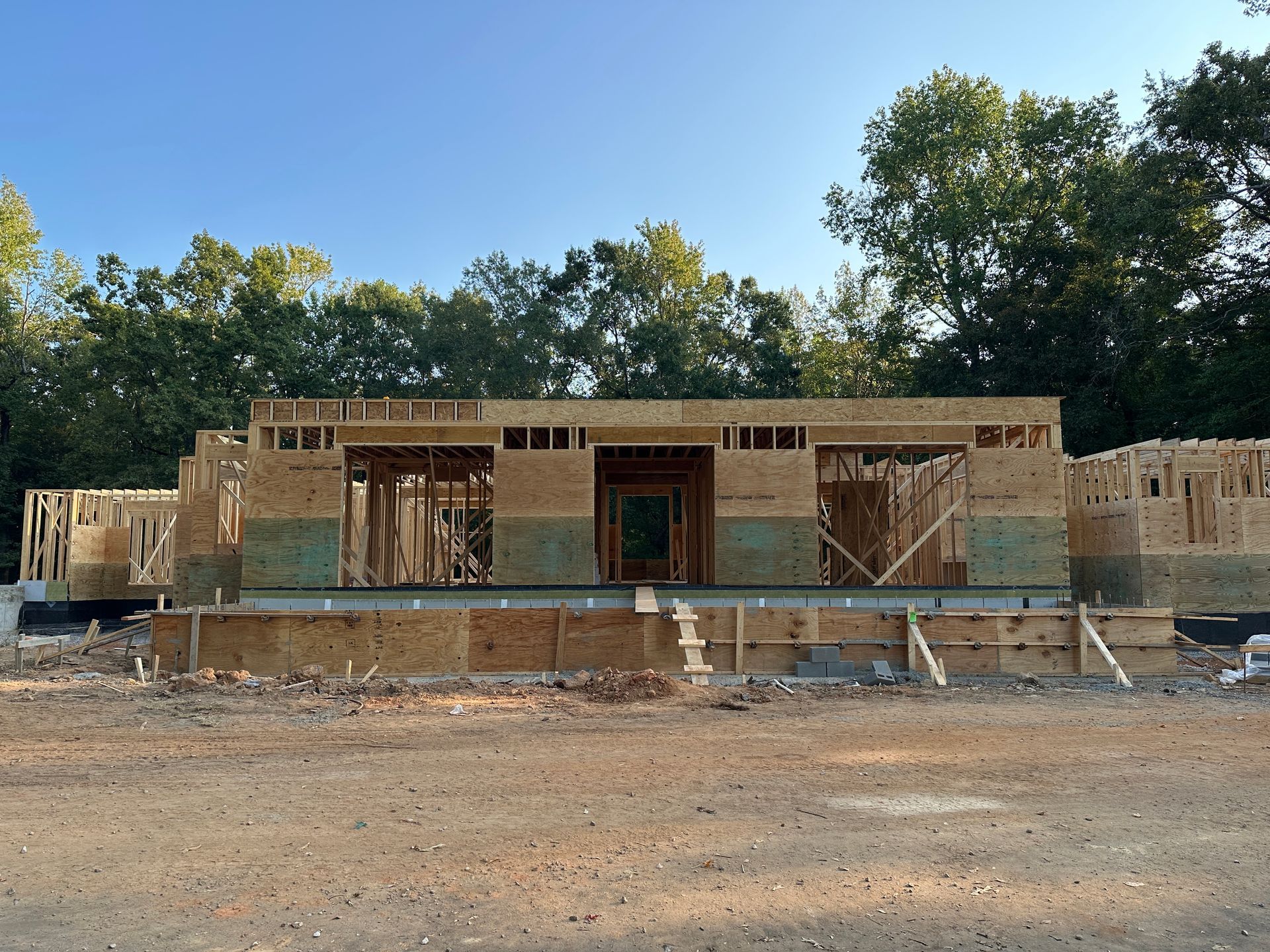 Wooden house under construction with framed walls against a backdrop of trees.