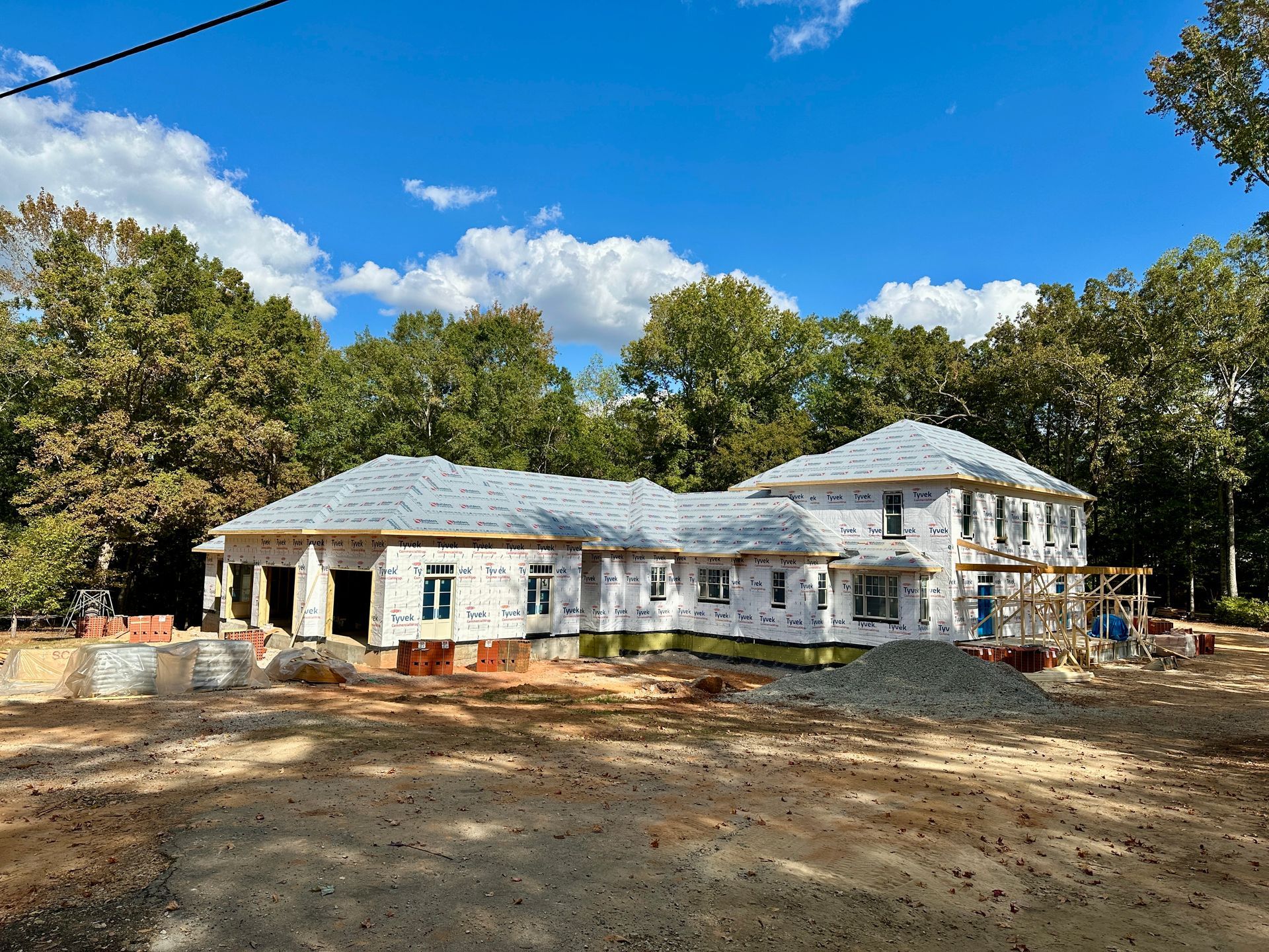 House under construction, exterior view, with blue sky and trees in the background.