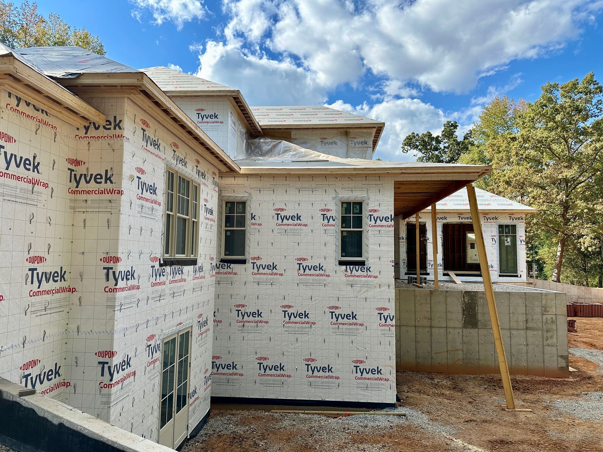 House under construction, covered in Tyvek, windows installed, blue sky with clouds.