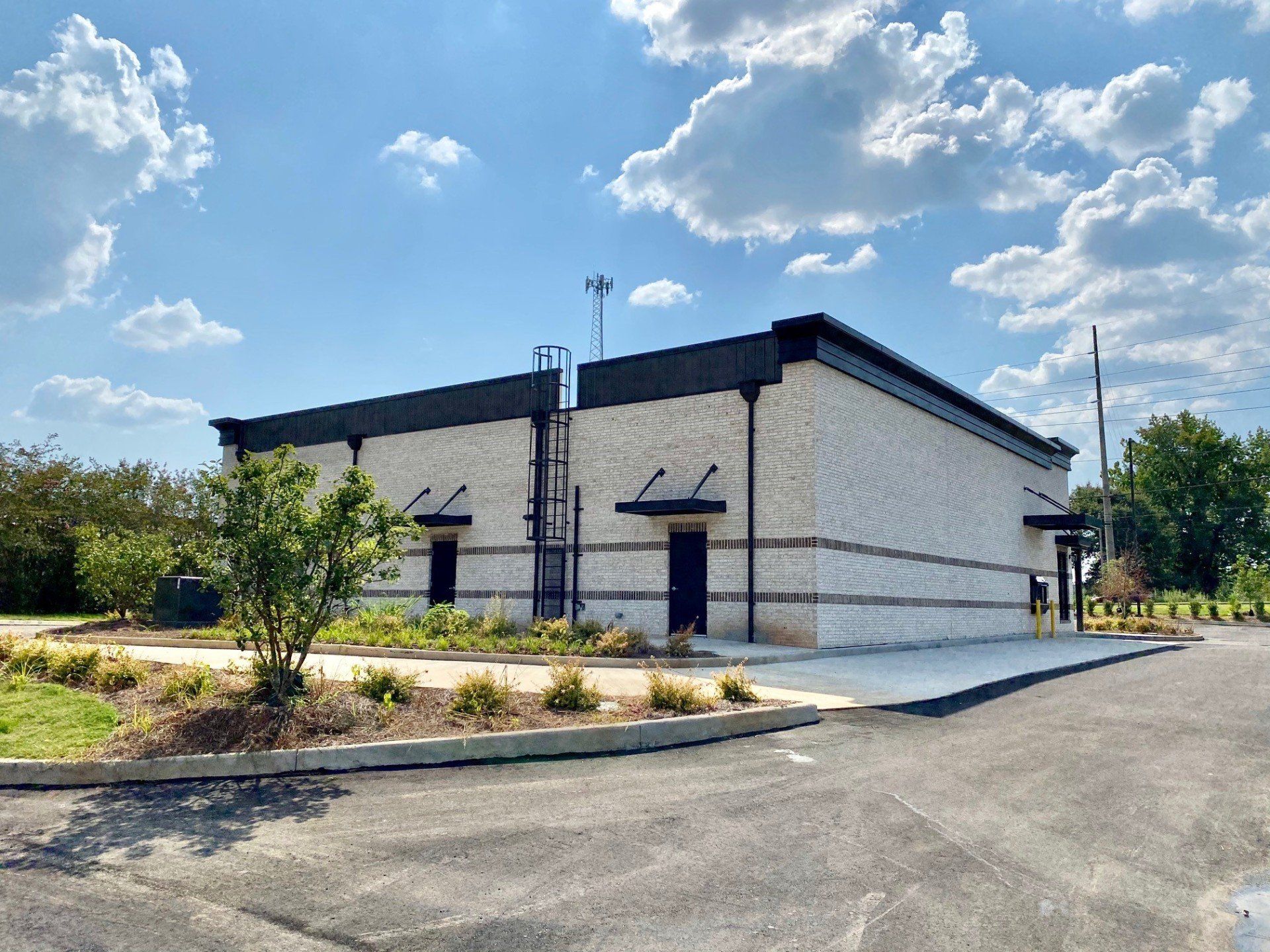 A large white building with a black roof is sitting in the middle of a parking lot.