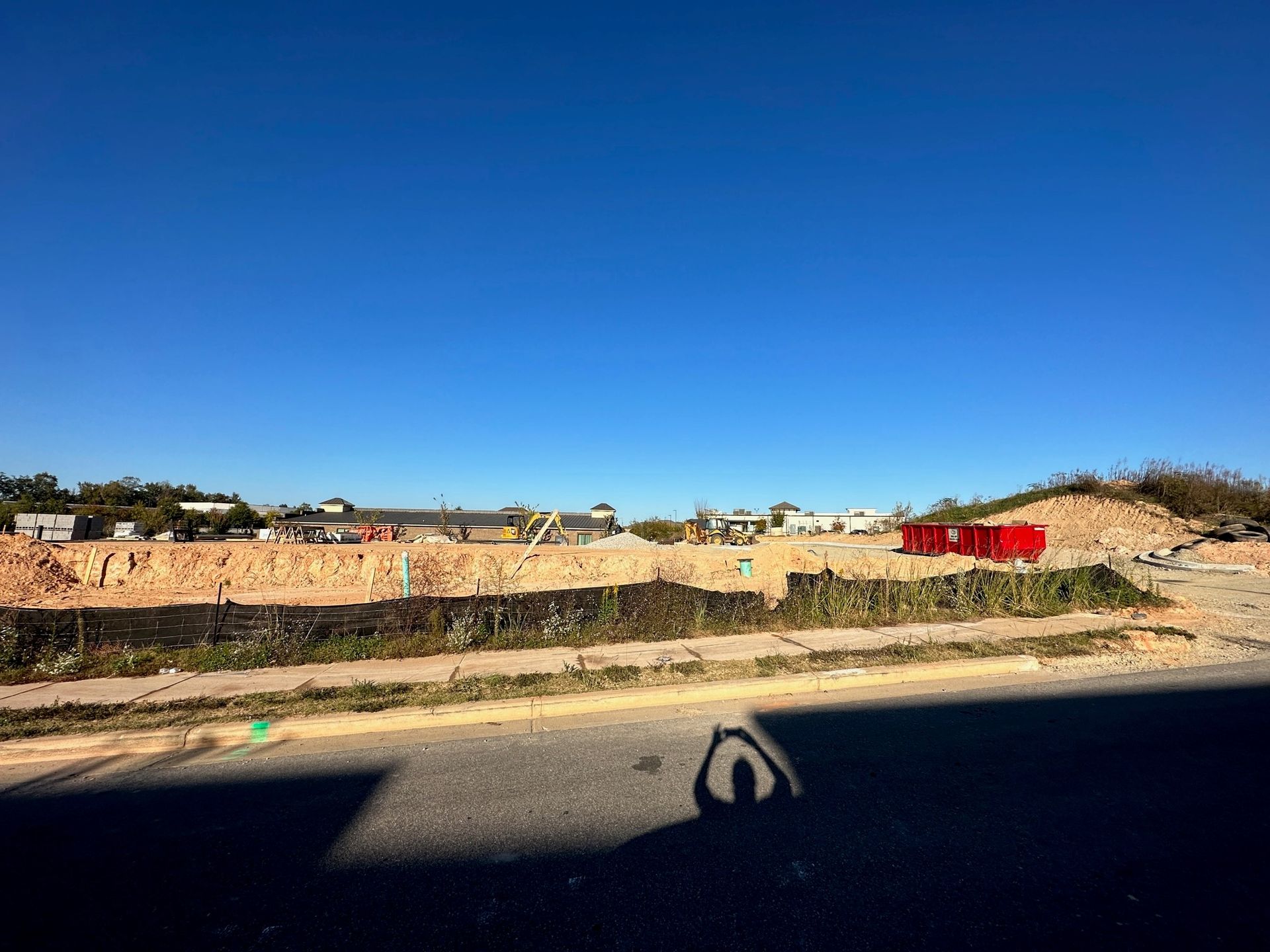 A shadow of a person is cast on the side of a road in front of a construction site.