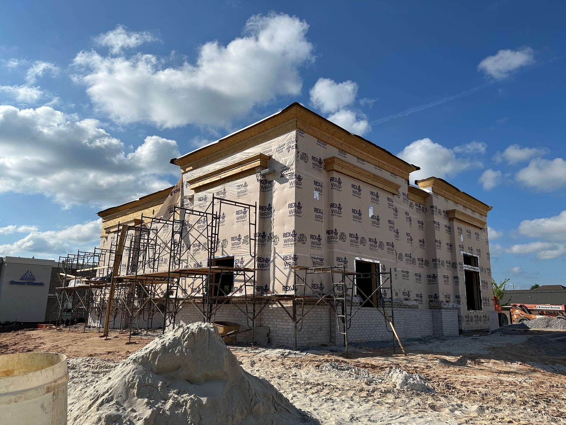 A large building under construction with scaffolding around it and a pile of sand in front of it.