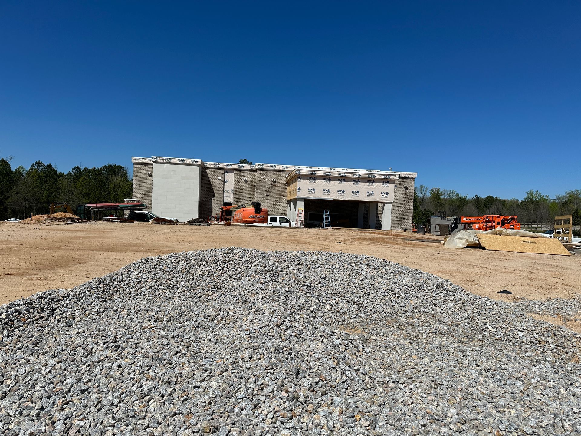 A large building is being built in a field with a pile of gravel in front of it.