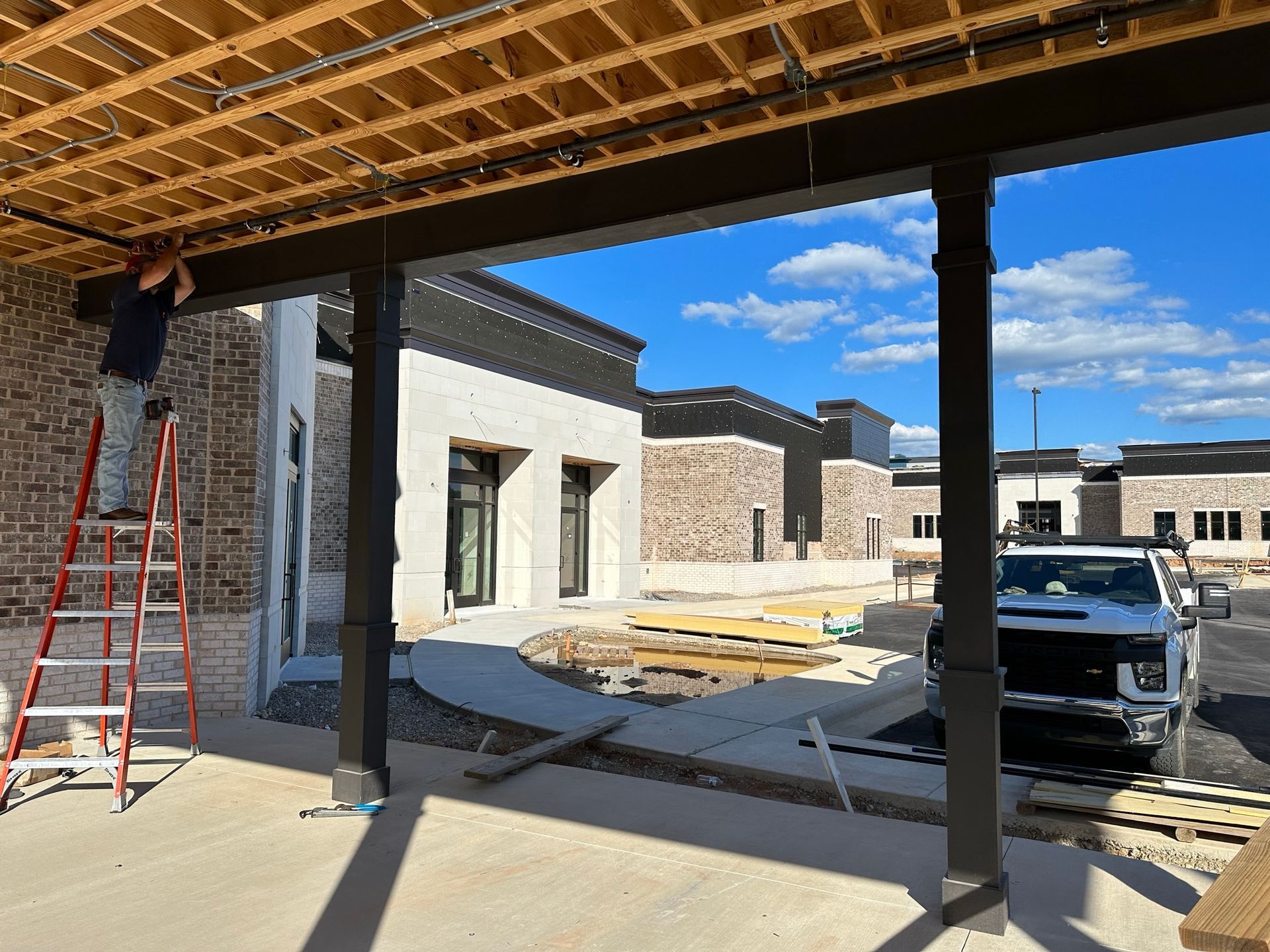 A man on a ladder is working on the ceiling of a building under construction.