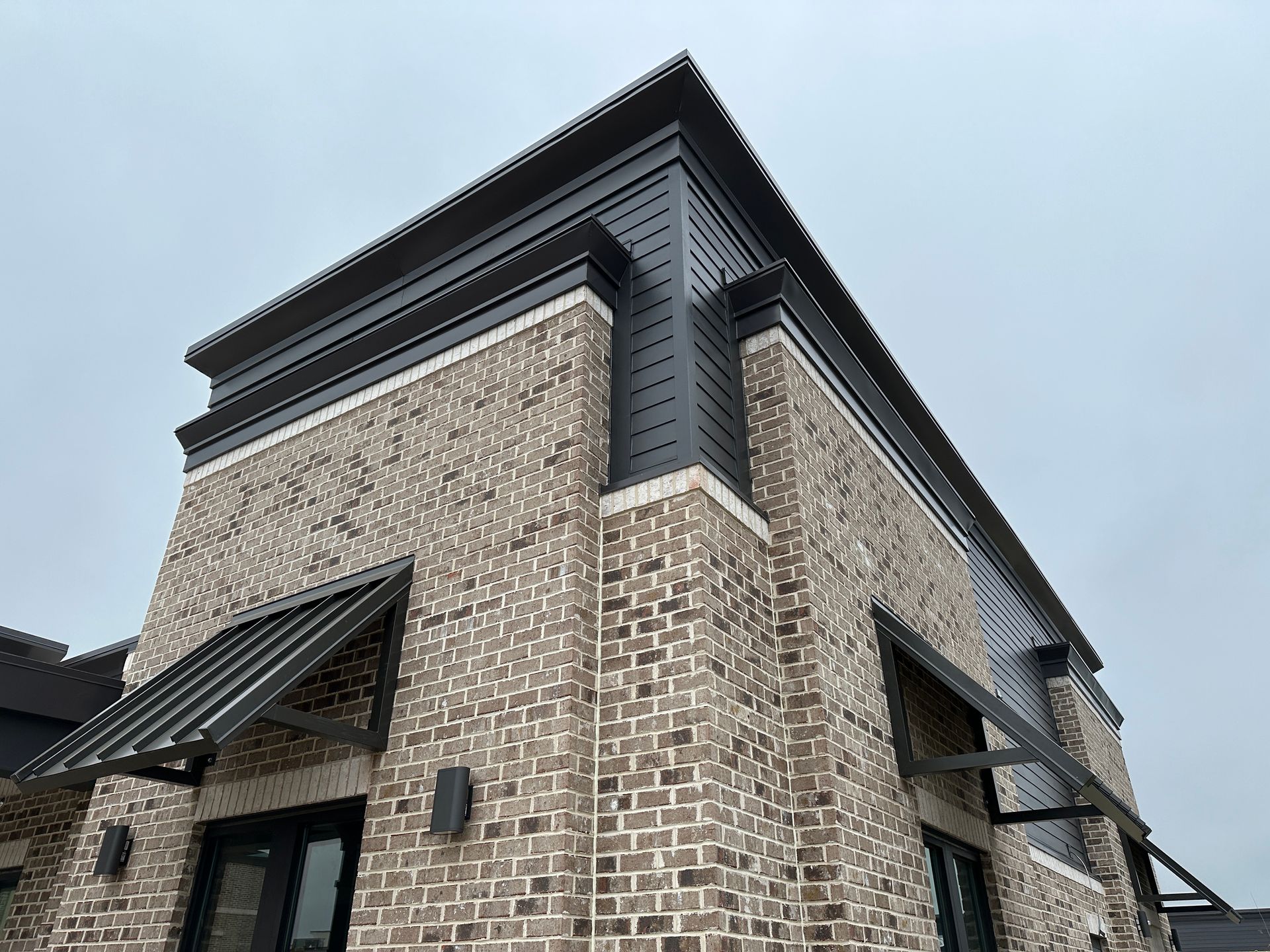 A brick building with a black roof and awnings on the side.