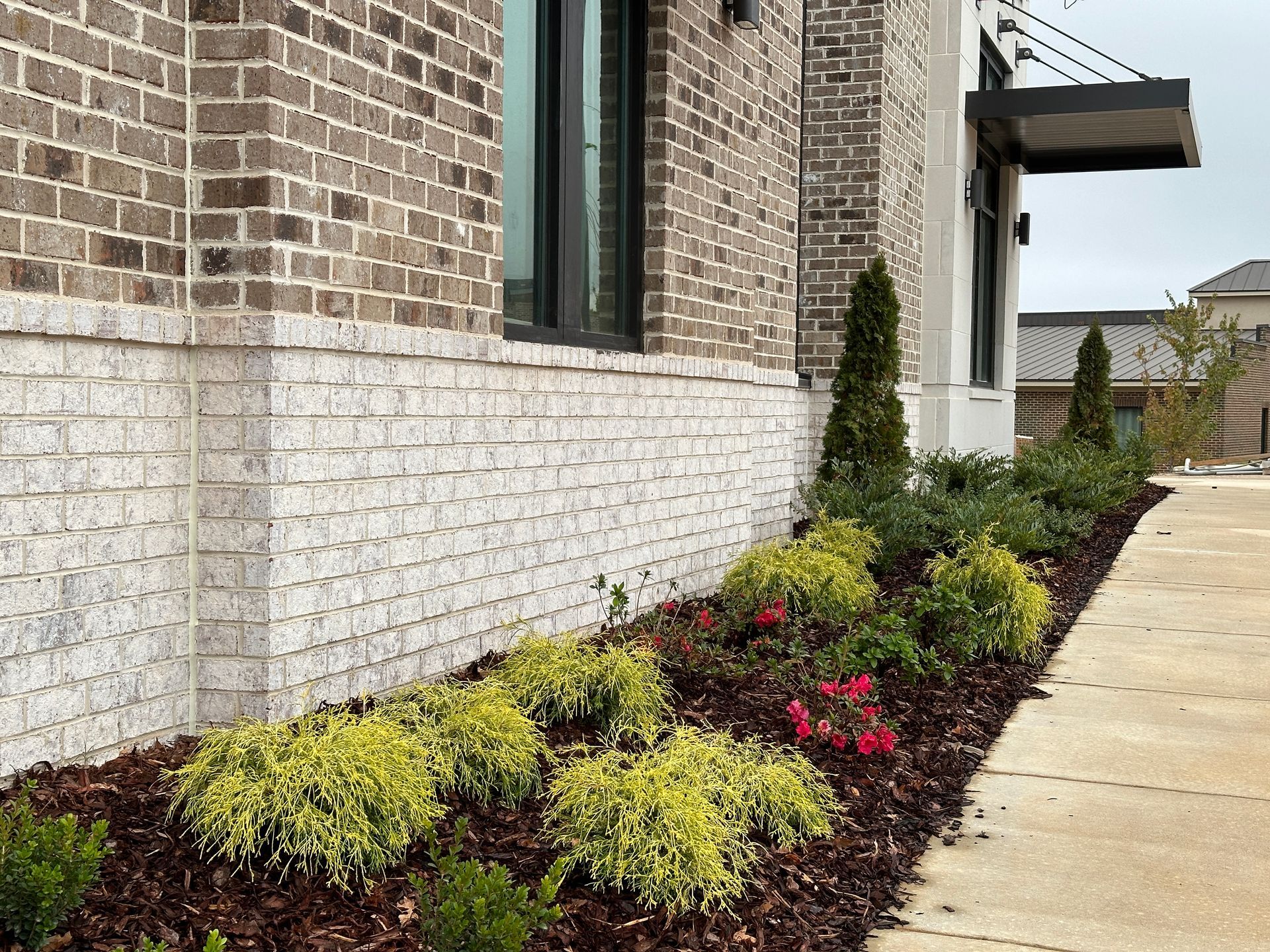 A brick building with a sidewalk and plants in front of it.