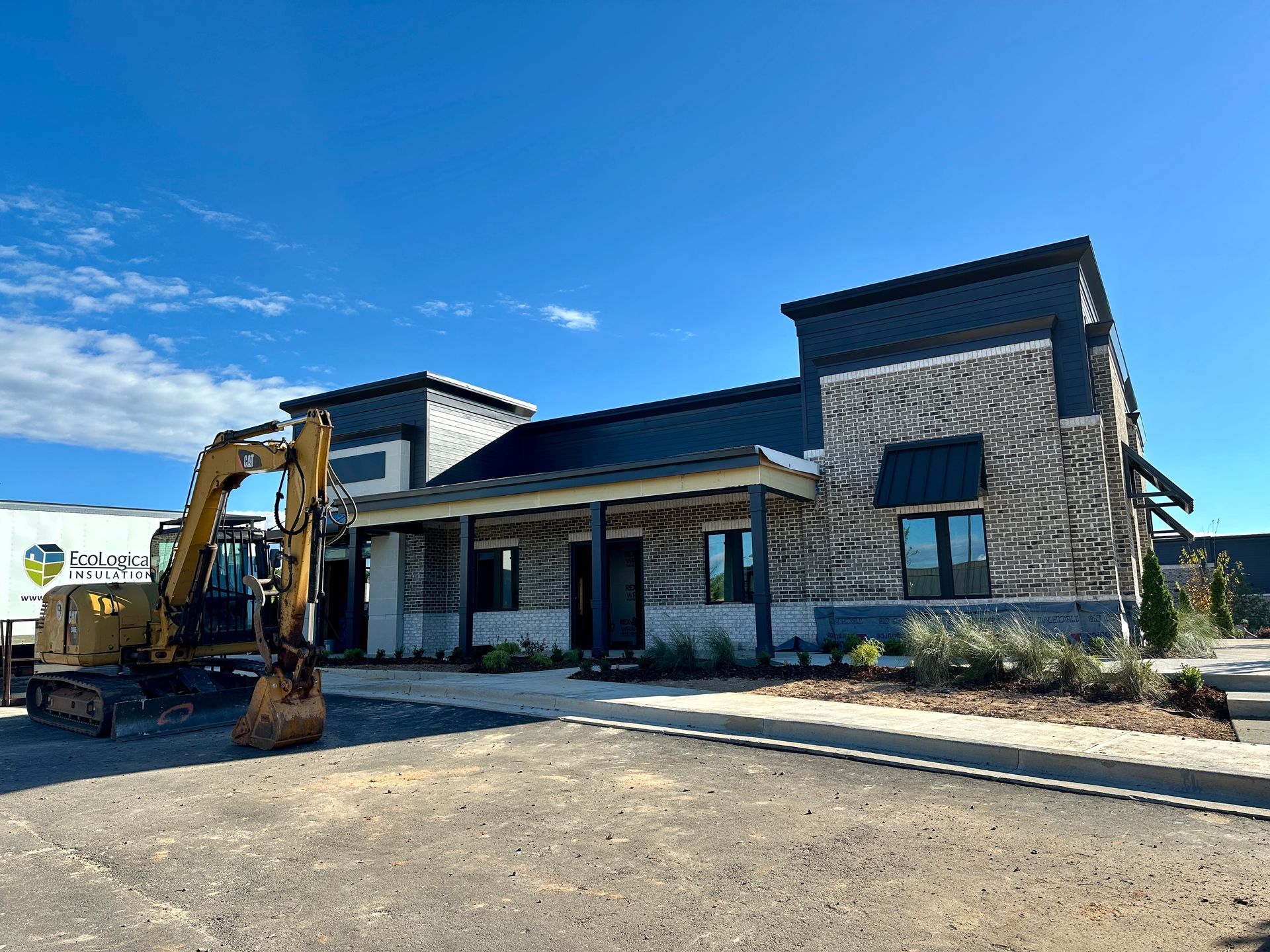A yellow excavator is parked in front of a brick building.