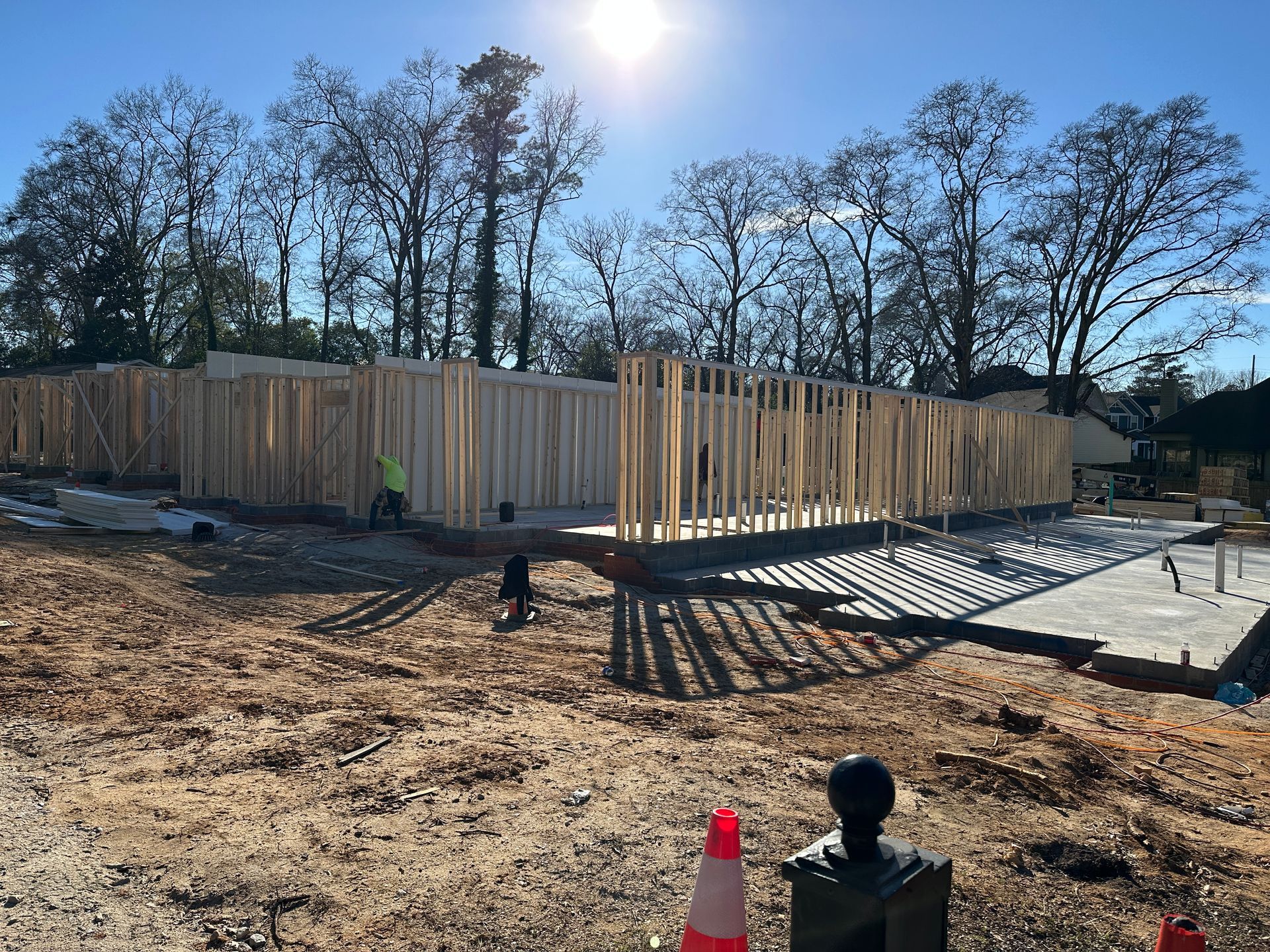 Construction site: Wooden frame of a building against a sunny sky; a worker is visible.