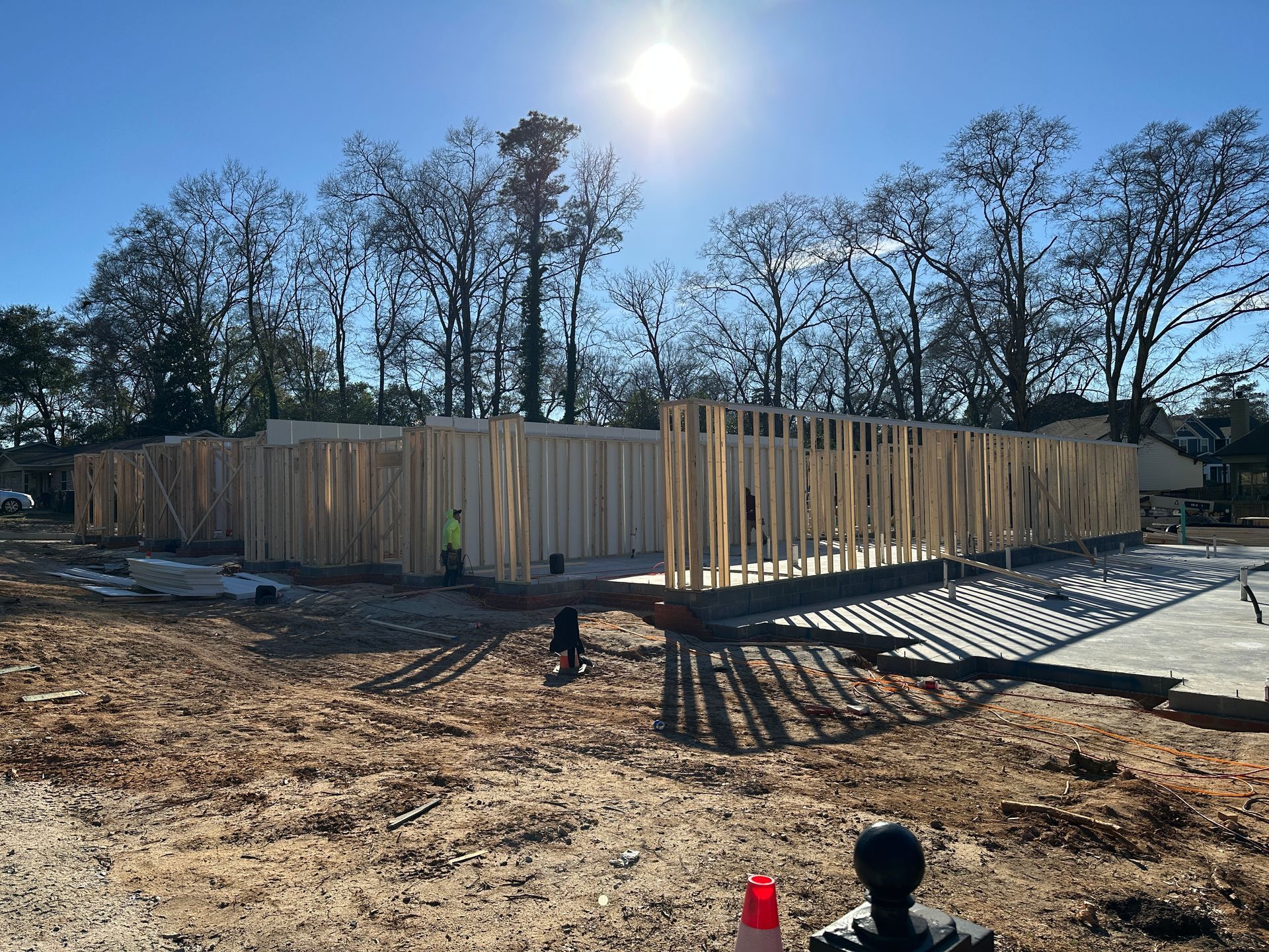 Wood frame construction of a building on a concrete foundation in a dirt lot, sunny day.