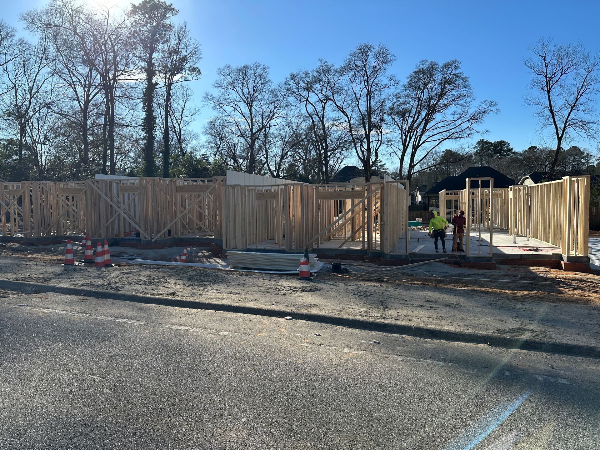 Construction site with wooden framing against a sunny, blue sky; workers present.