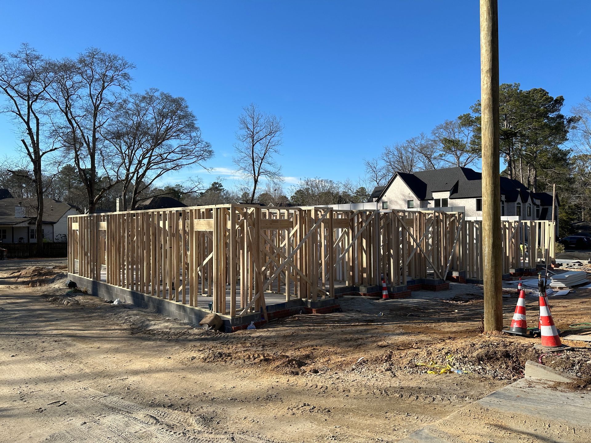 Wooden framework of a new house under construction on a dirt lot, clear blue sky overhead.