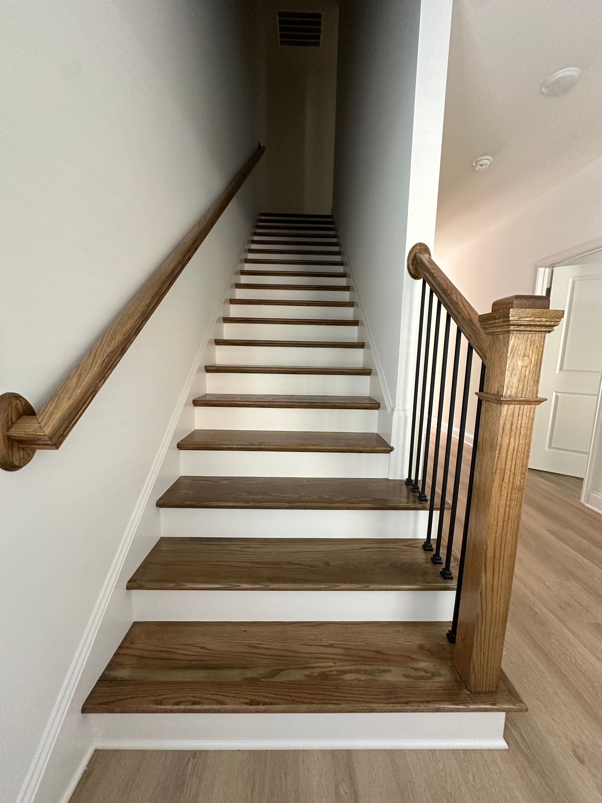 Staircase with dark wood treads, white risers, and a wooden handrail in a narrow hallway.