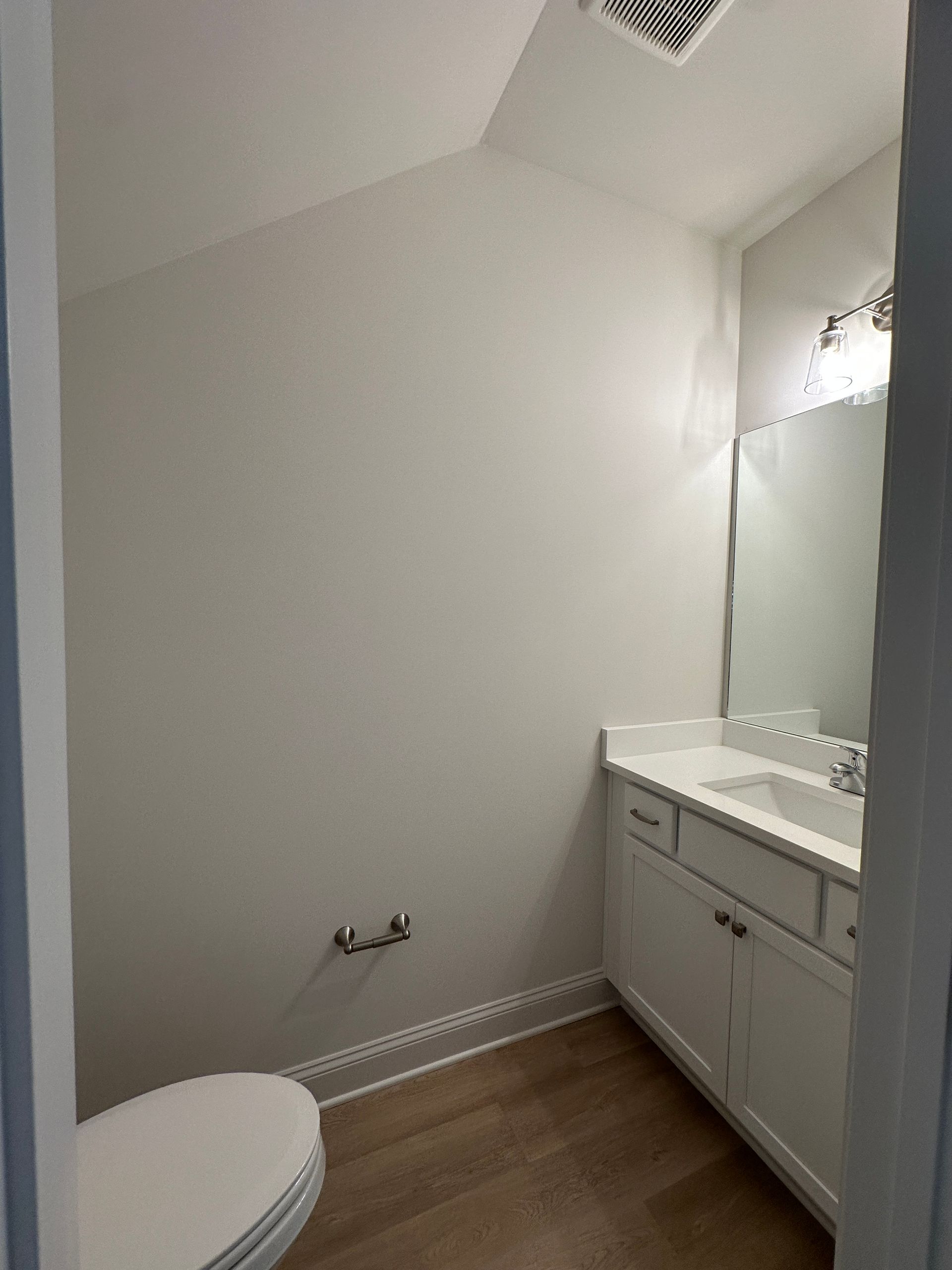 Small bathroom with a toilet, vanity sink, mirror, and wood-look floor.