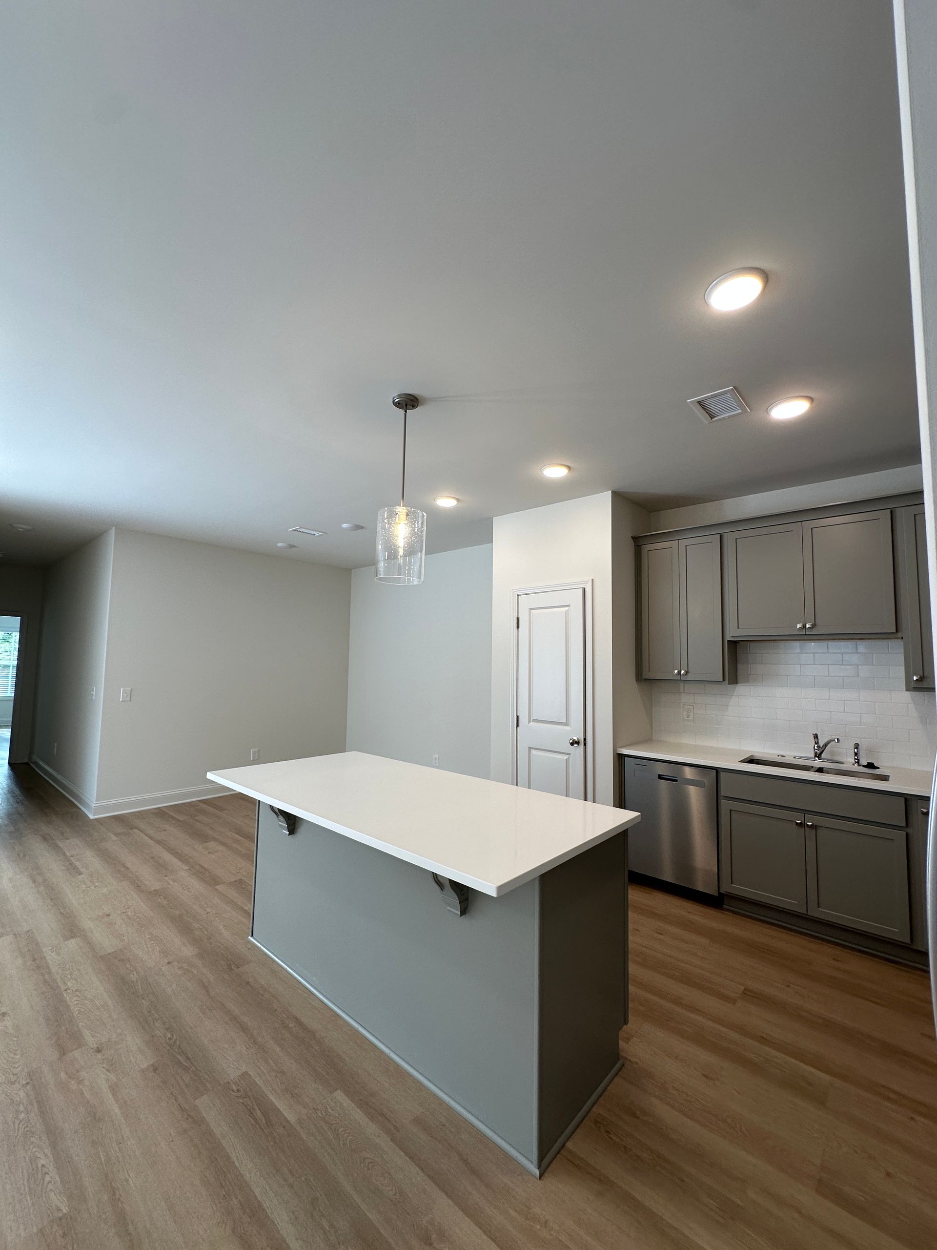 Empty modern kitchen with white island, wood floors, gray cabinets, and recessed ceiling lights