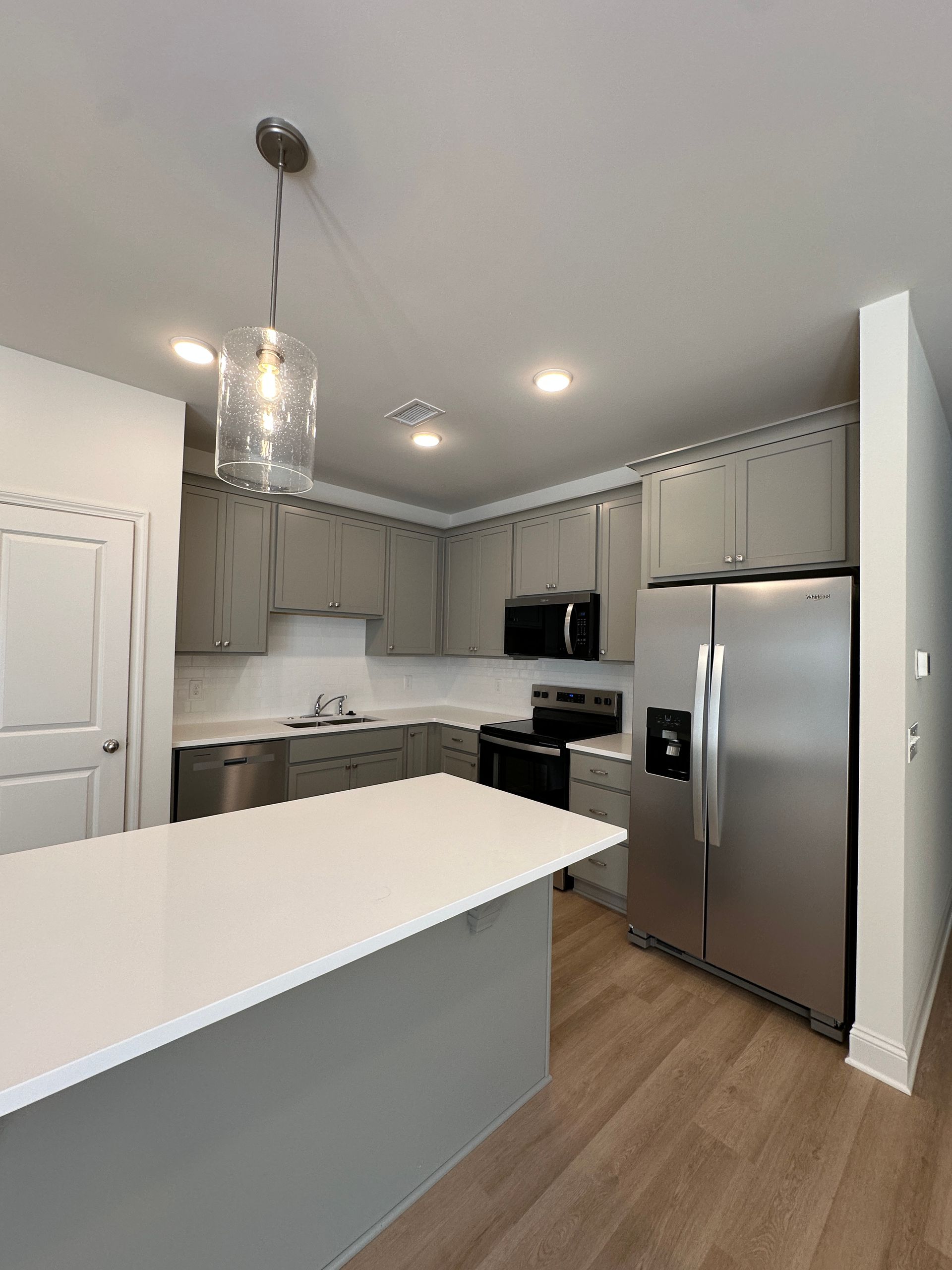 Modern kitchen with white island, gray cabinets, stainless steel appliances, and wood flooring