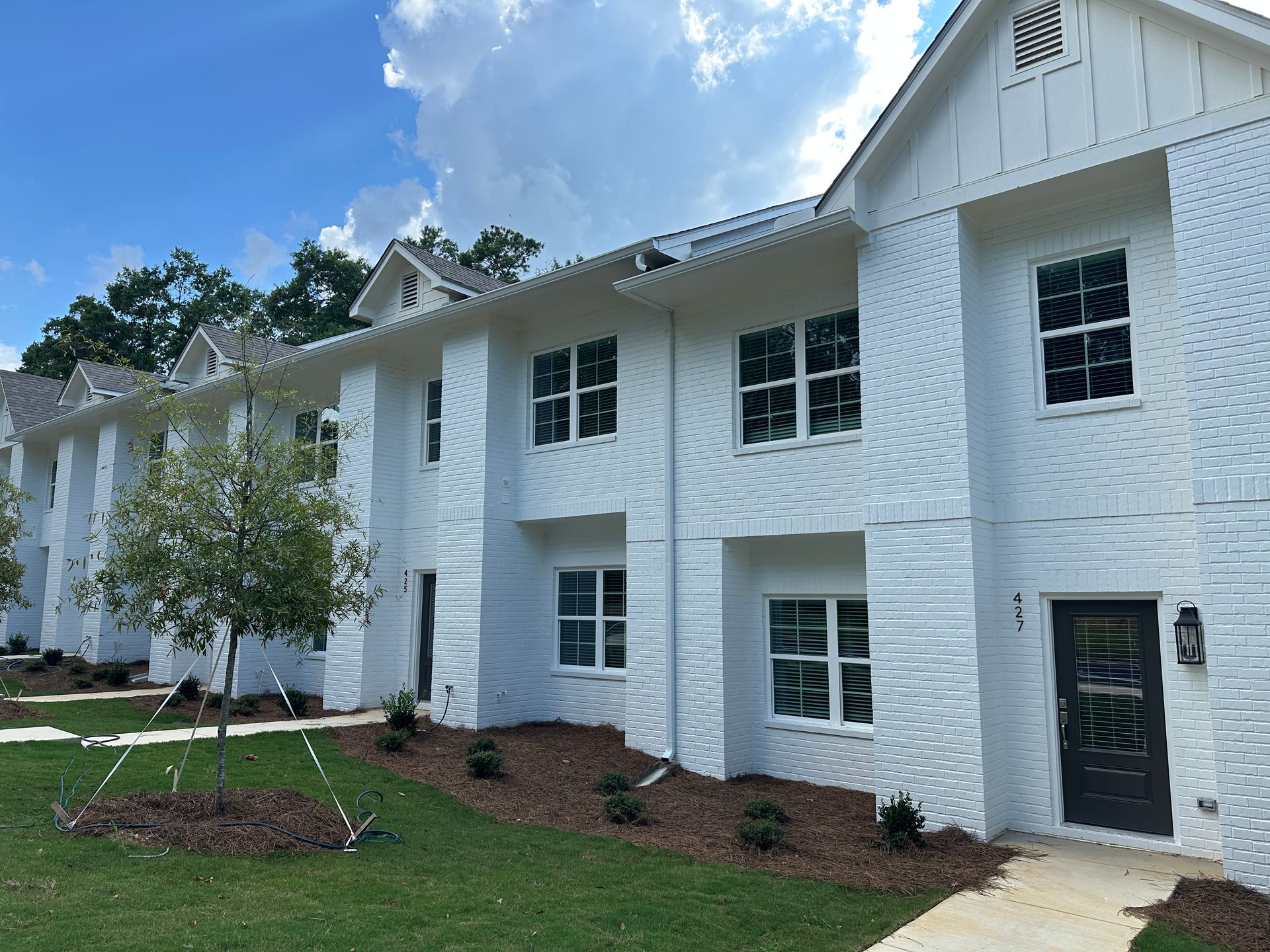 White two-story apartment building with black windows, a dark front door, and landscaped lawn under a blue sky