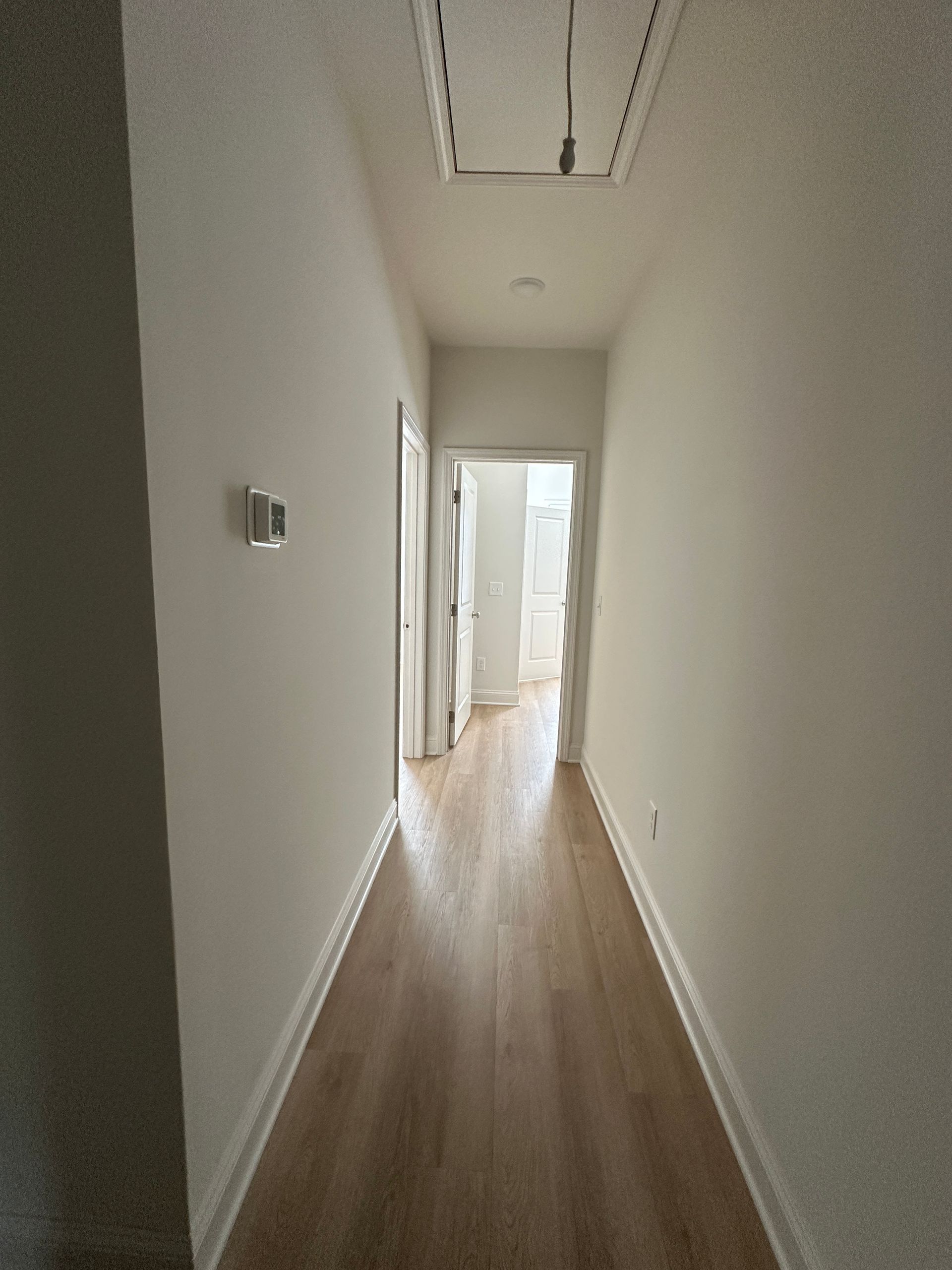 Narrow white hallway with wood floors and an open door leading to a bright room
