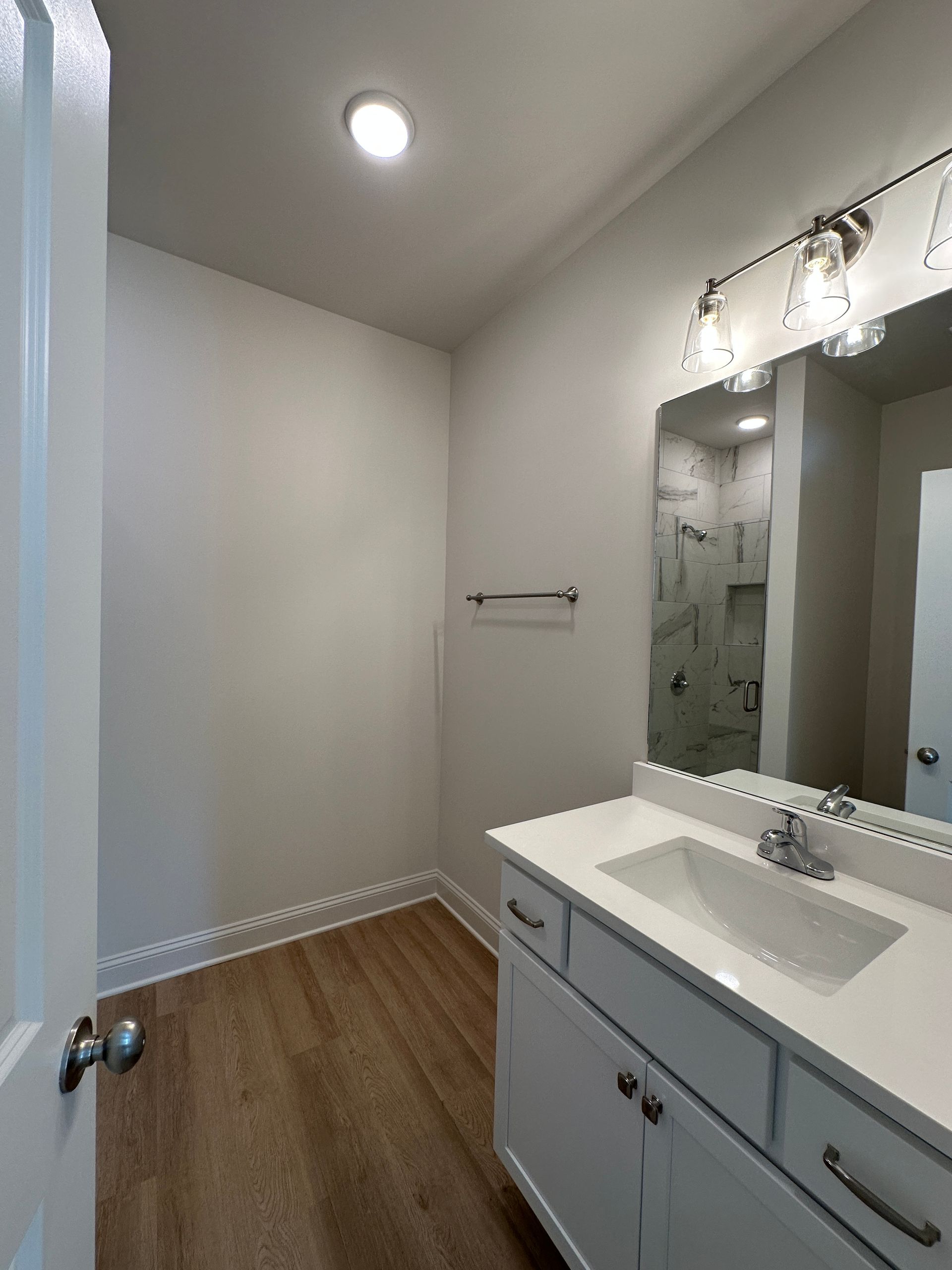 Small bathroom vanity with mirror, white sink, towel bar, and wood-look floor
