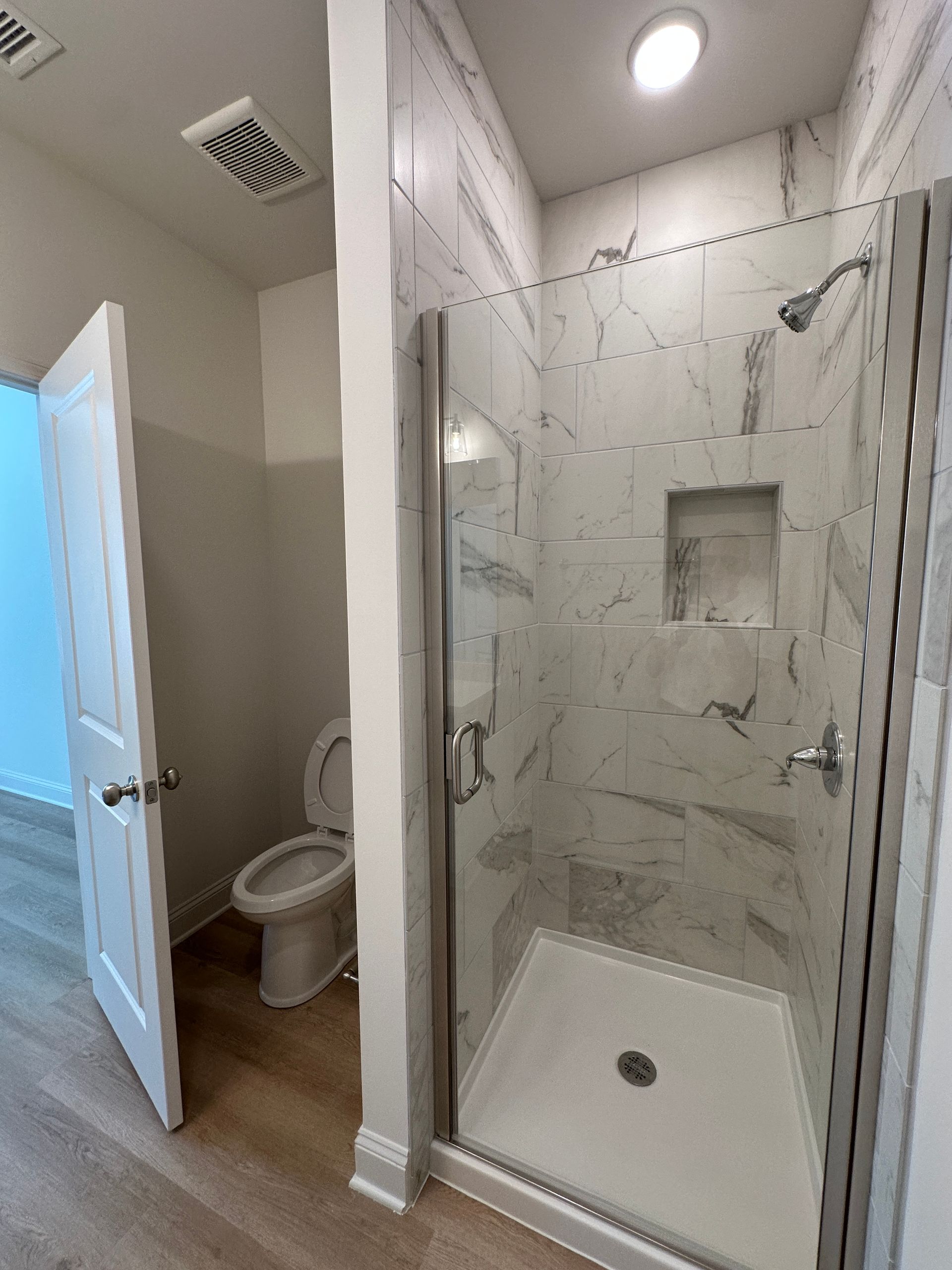 Bathroom with walk-in shower, white tile, glass door, and toilet visible through open door.
