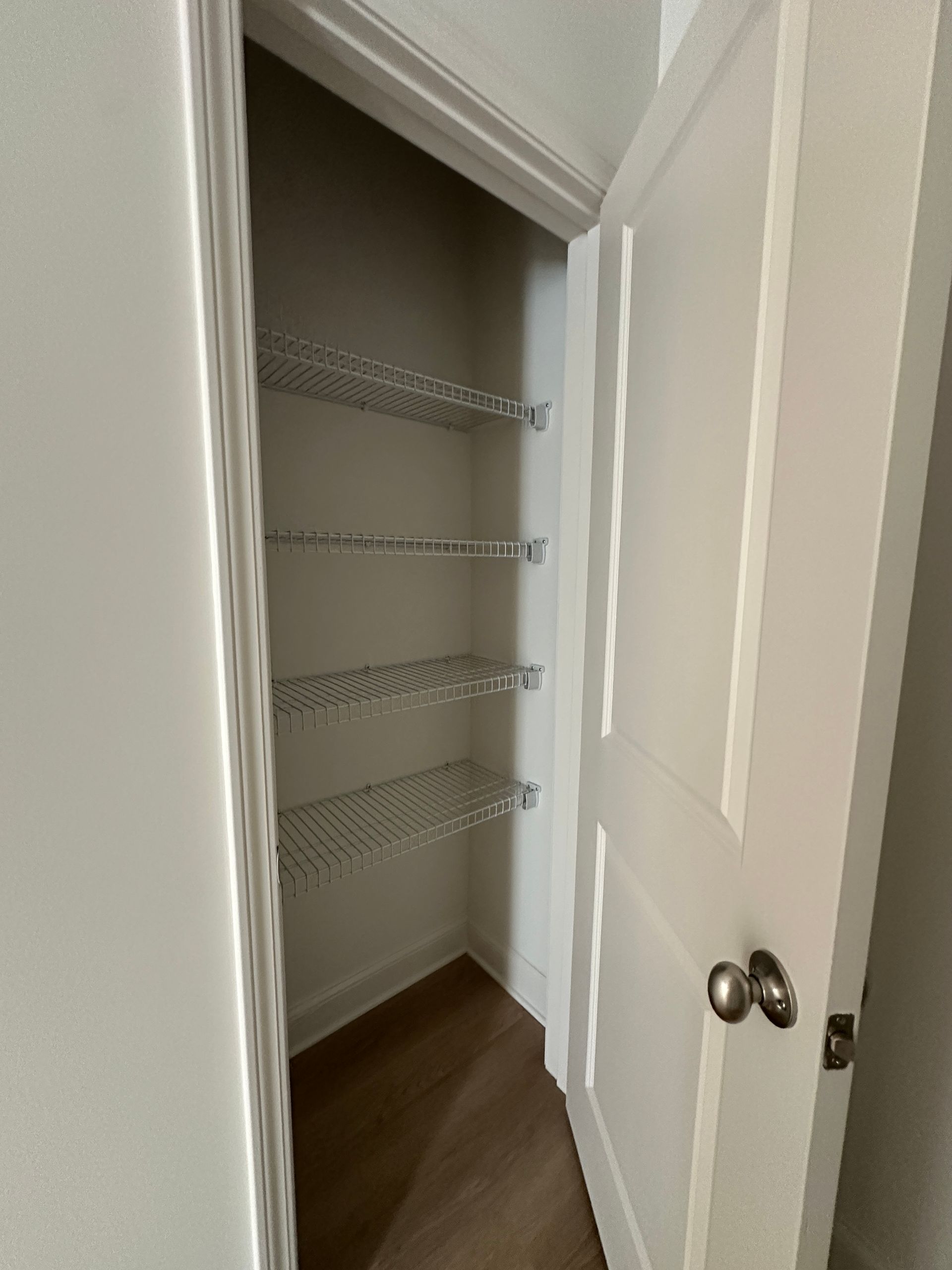 Open closet with white wire shelves and dark wood floor, door partially open.