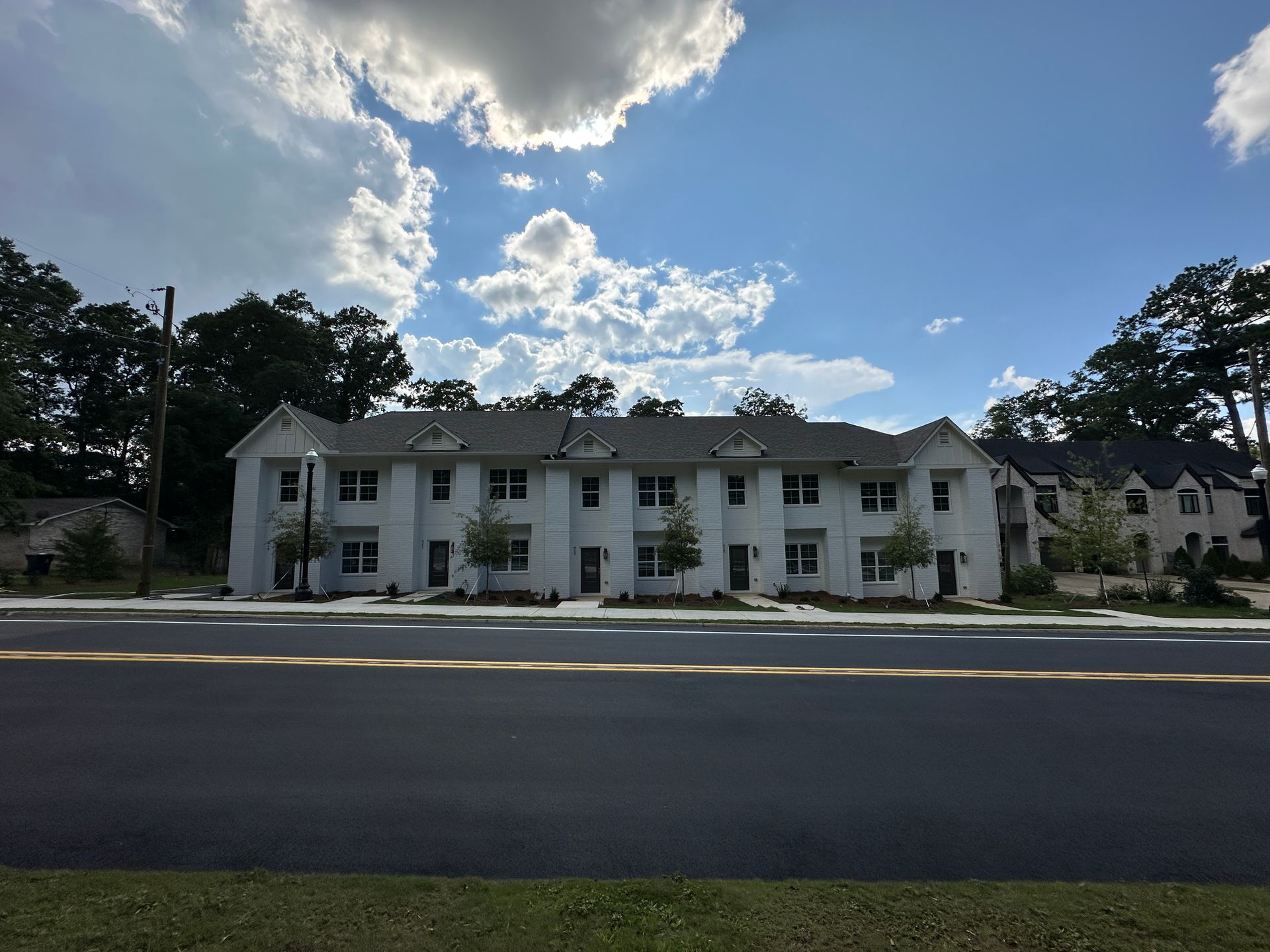 White two-story building with columns across a road under a partly cloudy blue sky