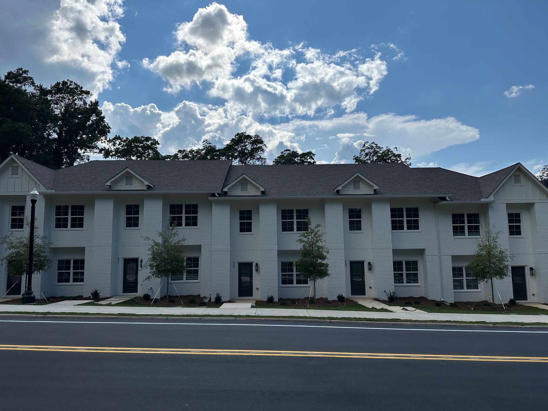 White apartment building with dormer windows under a cloudy blue sky, viewed from across the street
