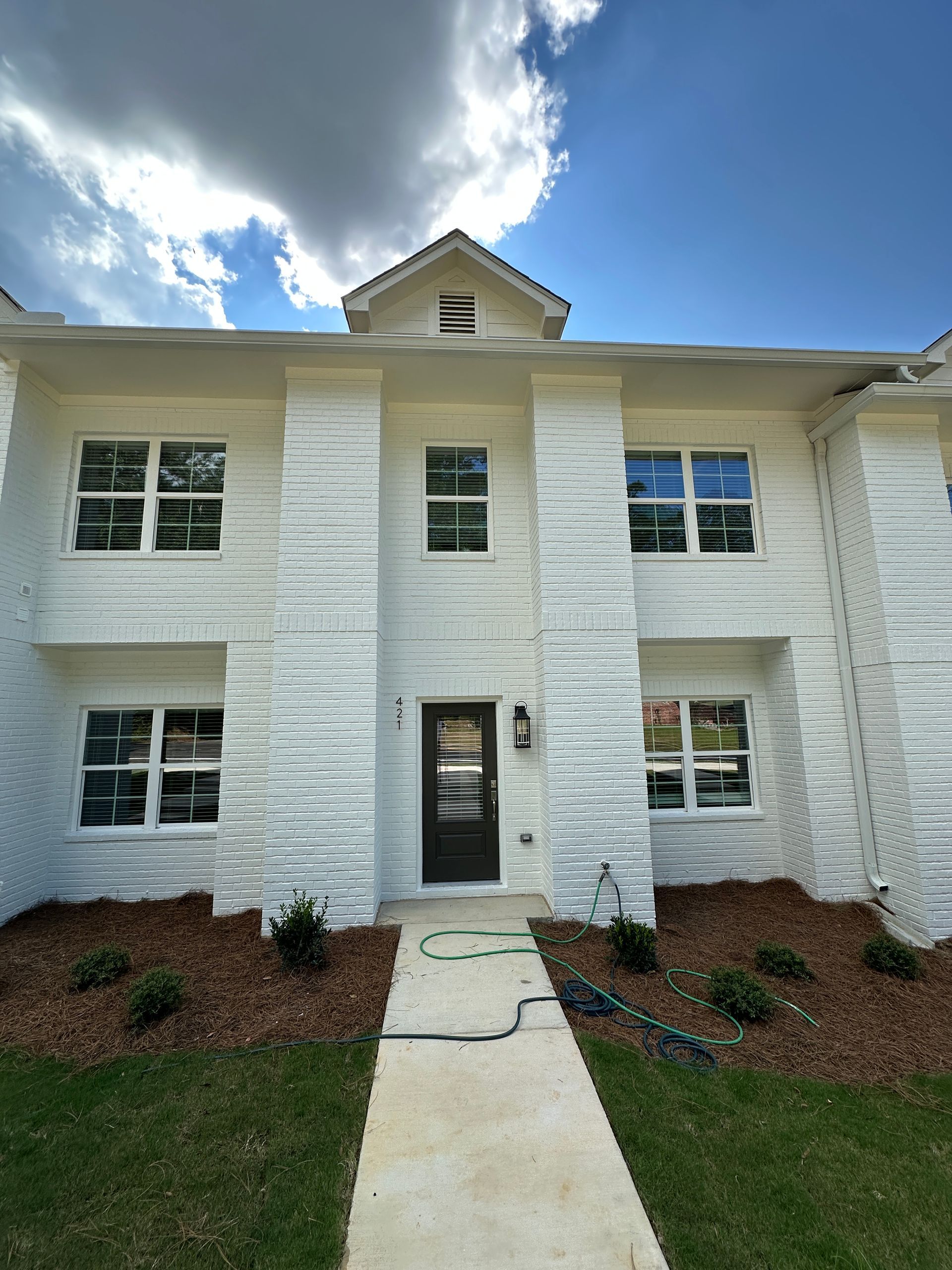 Two-story white townhouse with a central front door, windows, and a concrete walkway under a blue sky