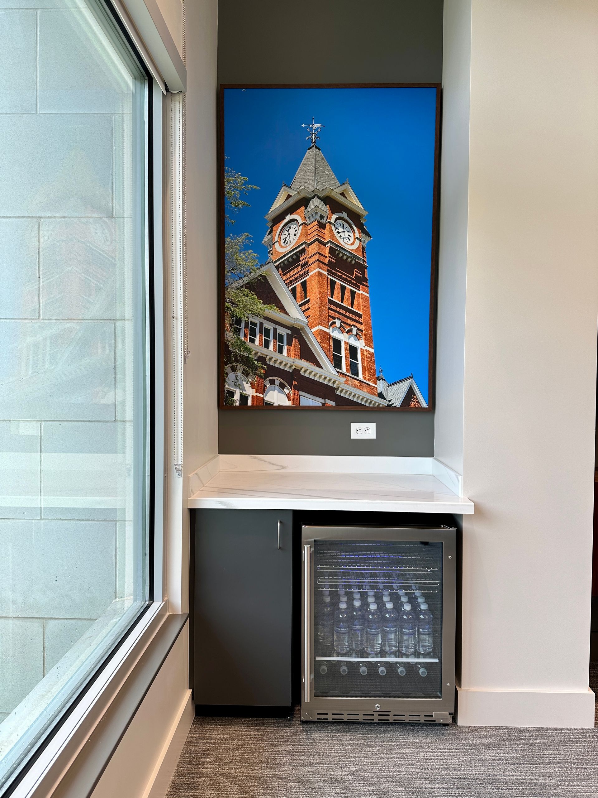 There is a picture of a clock tower on the wall above a refrigerator.
