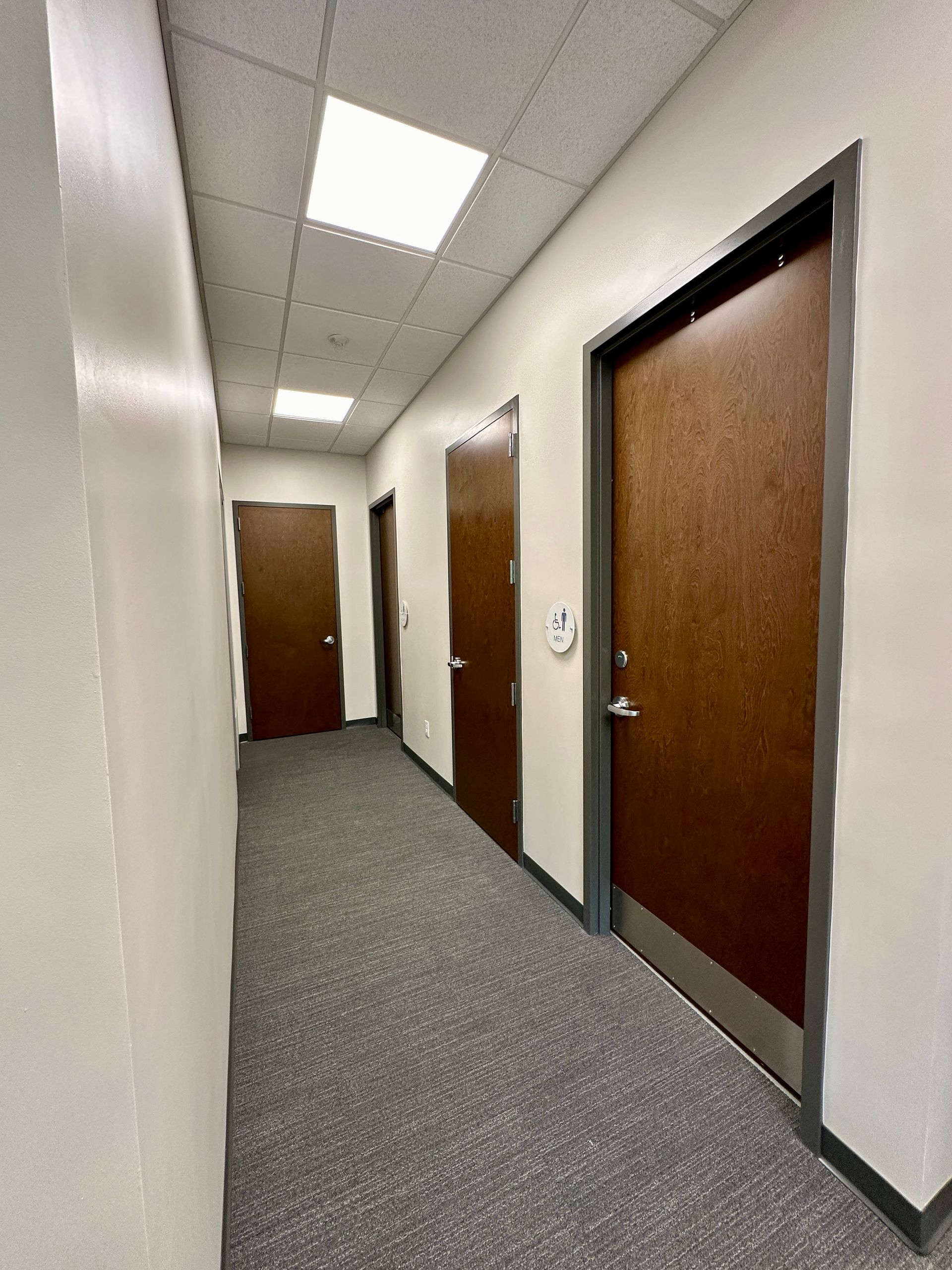 A long hallway with a lot of doors and a clock on the wall.