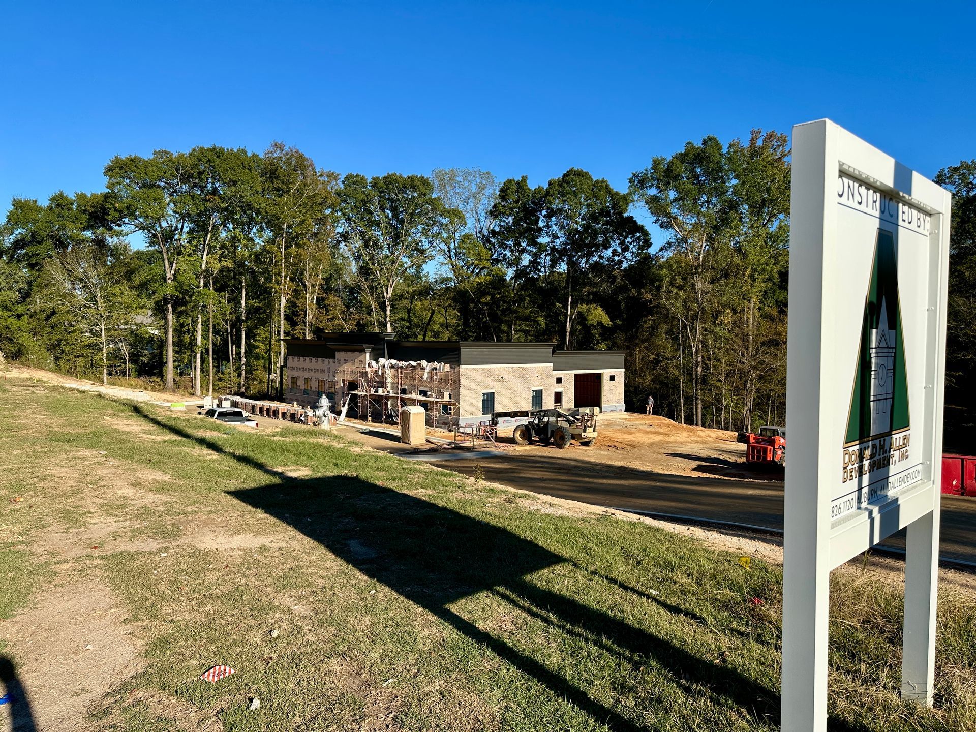 Construction site with building frame, surrounded by trees and a sign.