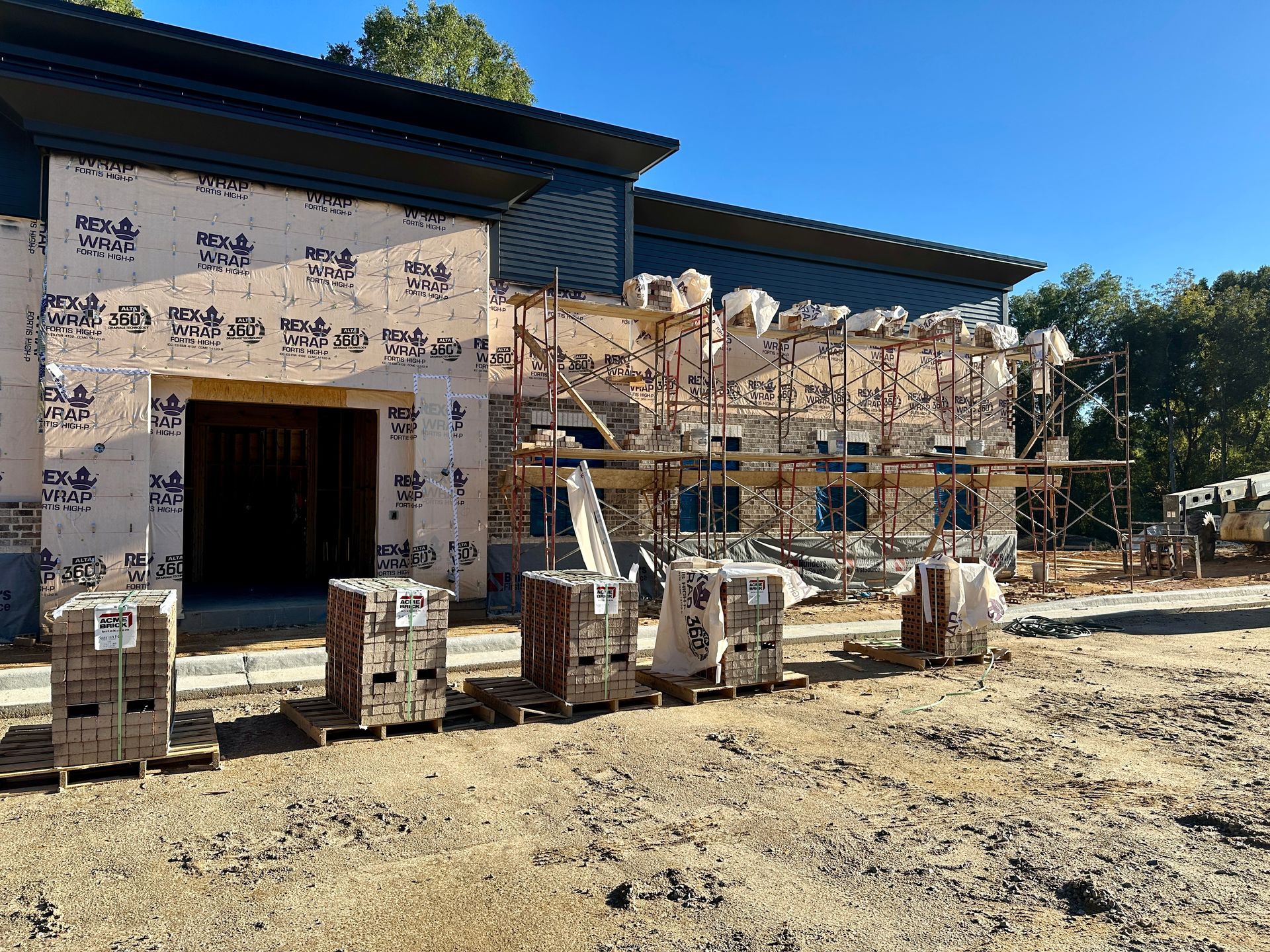 Building under construction with scaffolding and stacks of bricks, blue sky.