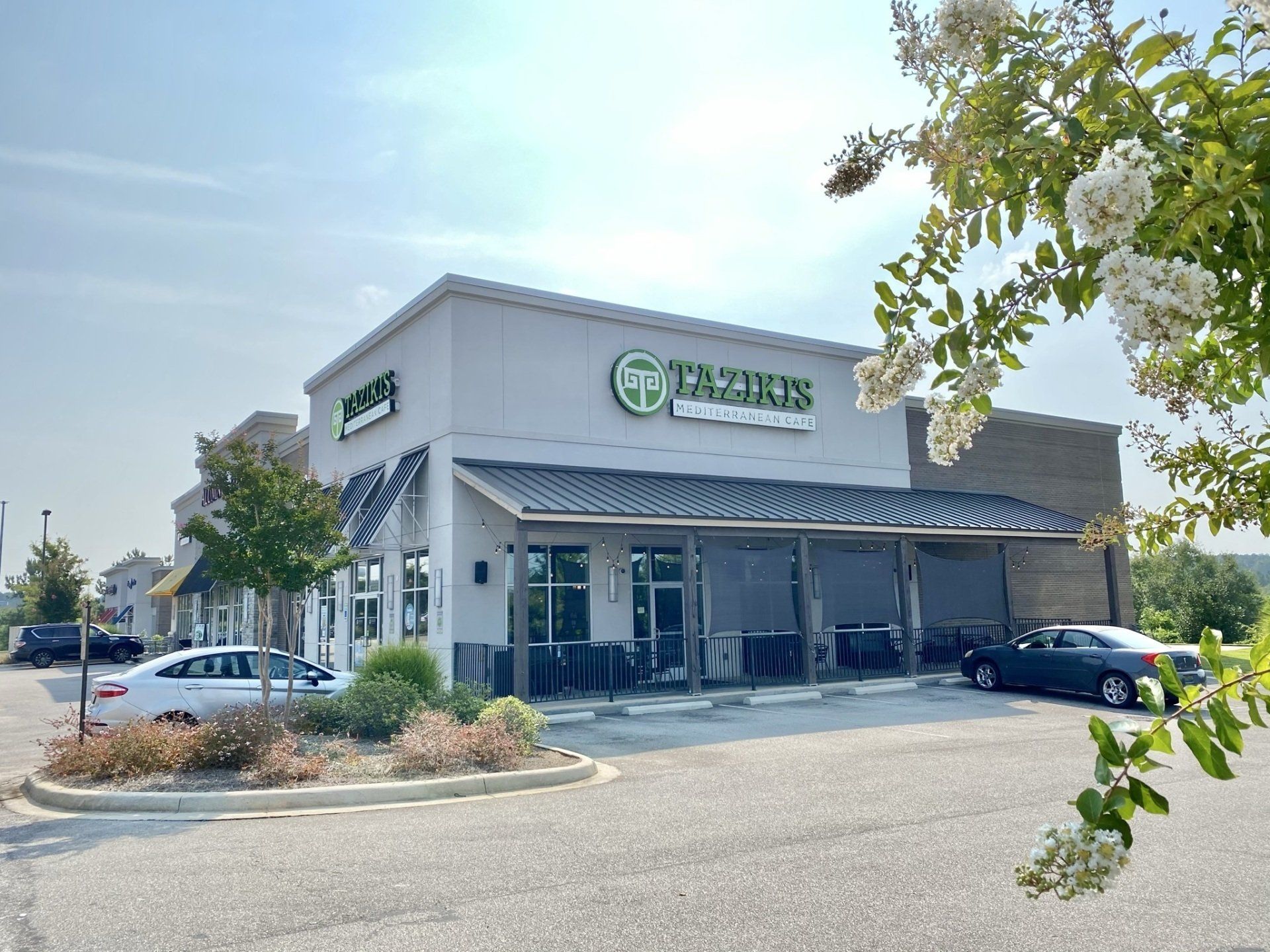 A white car is parked in front of a taziki 's restaurant.