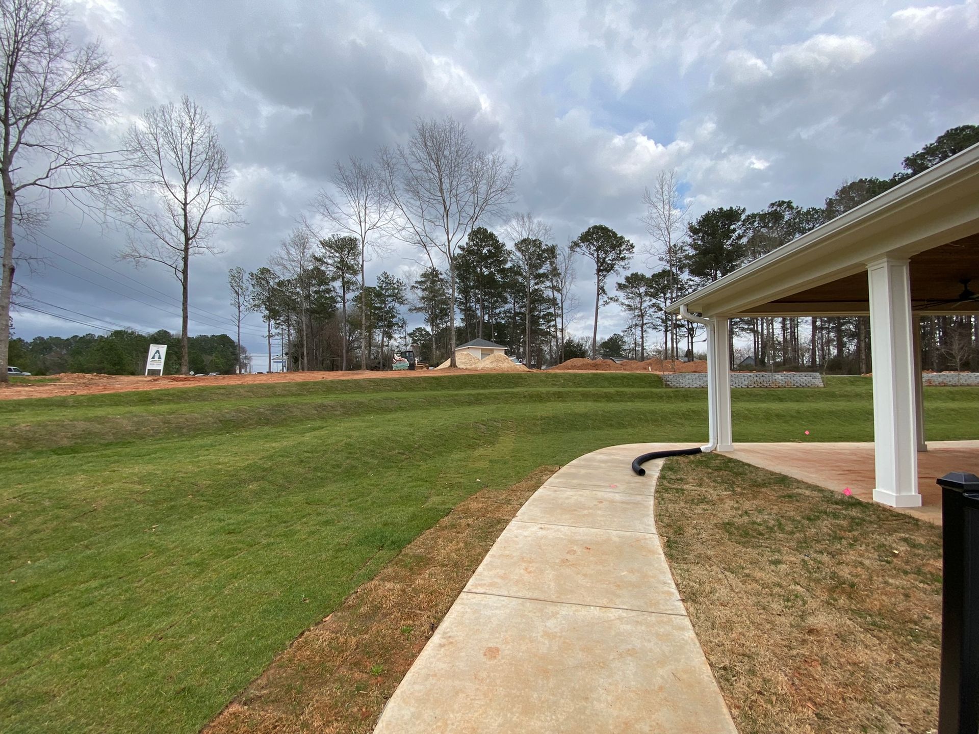 A sidewalk leading to a grassy field with a pavilion in the background.