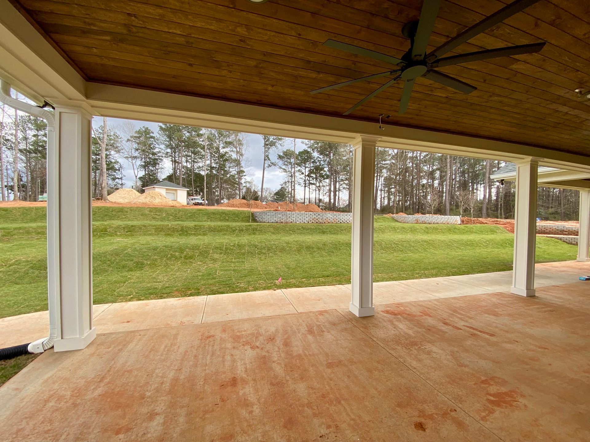 A large covered patio with a ceiling fan and a view of a grassy field.