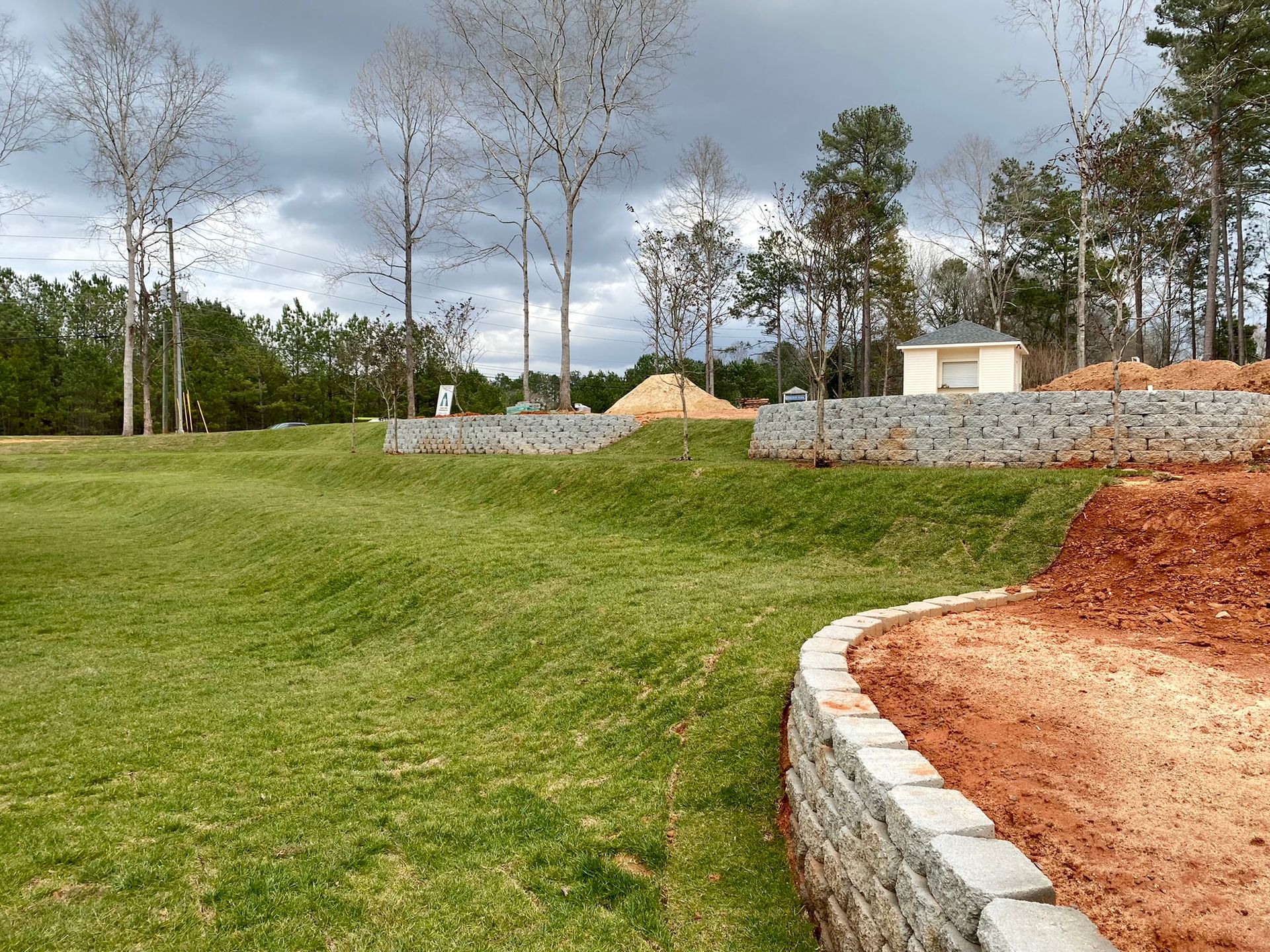A large grassy field with trees in the background and a stone wall in the foreground.