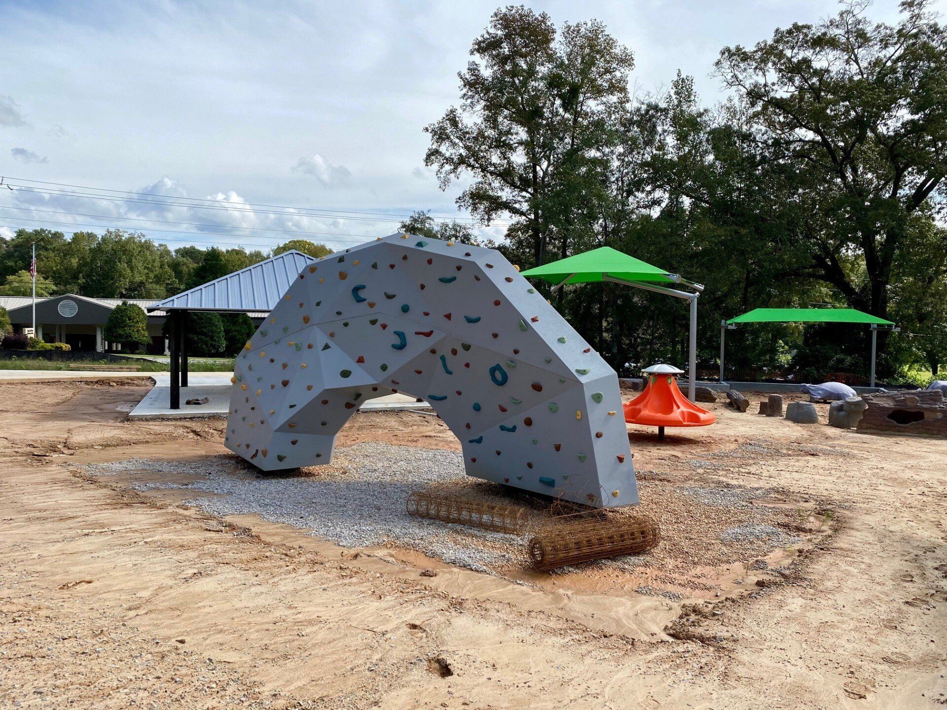 A large rock climbing wall is sitting in the middle of a playground.