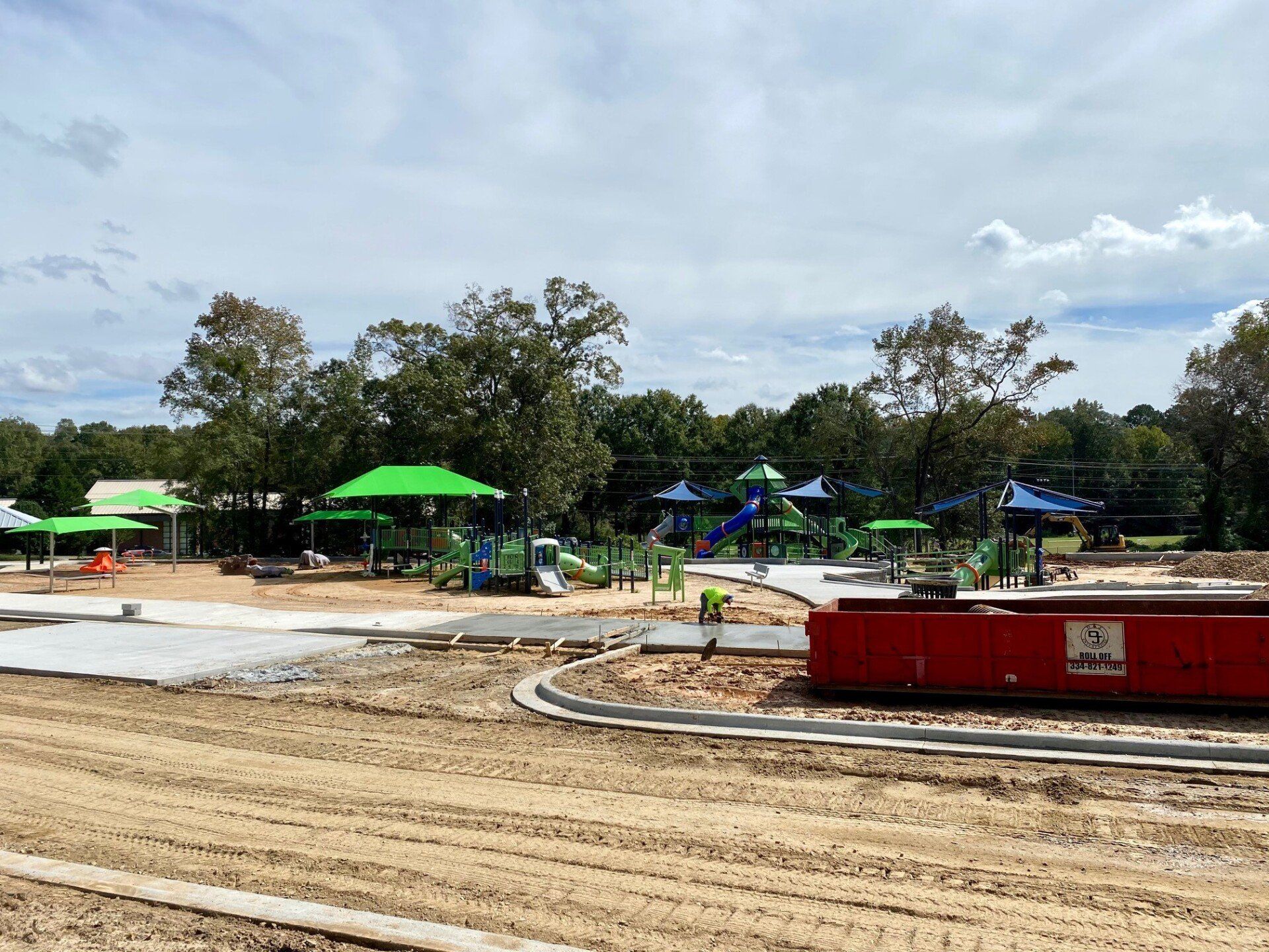 A playground is being built in a park with a red dumpster in the foreground.