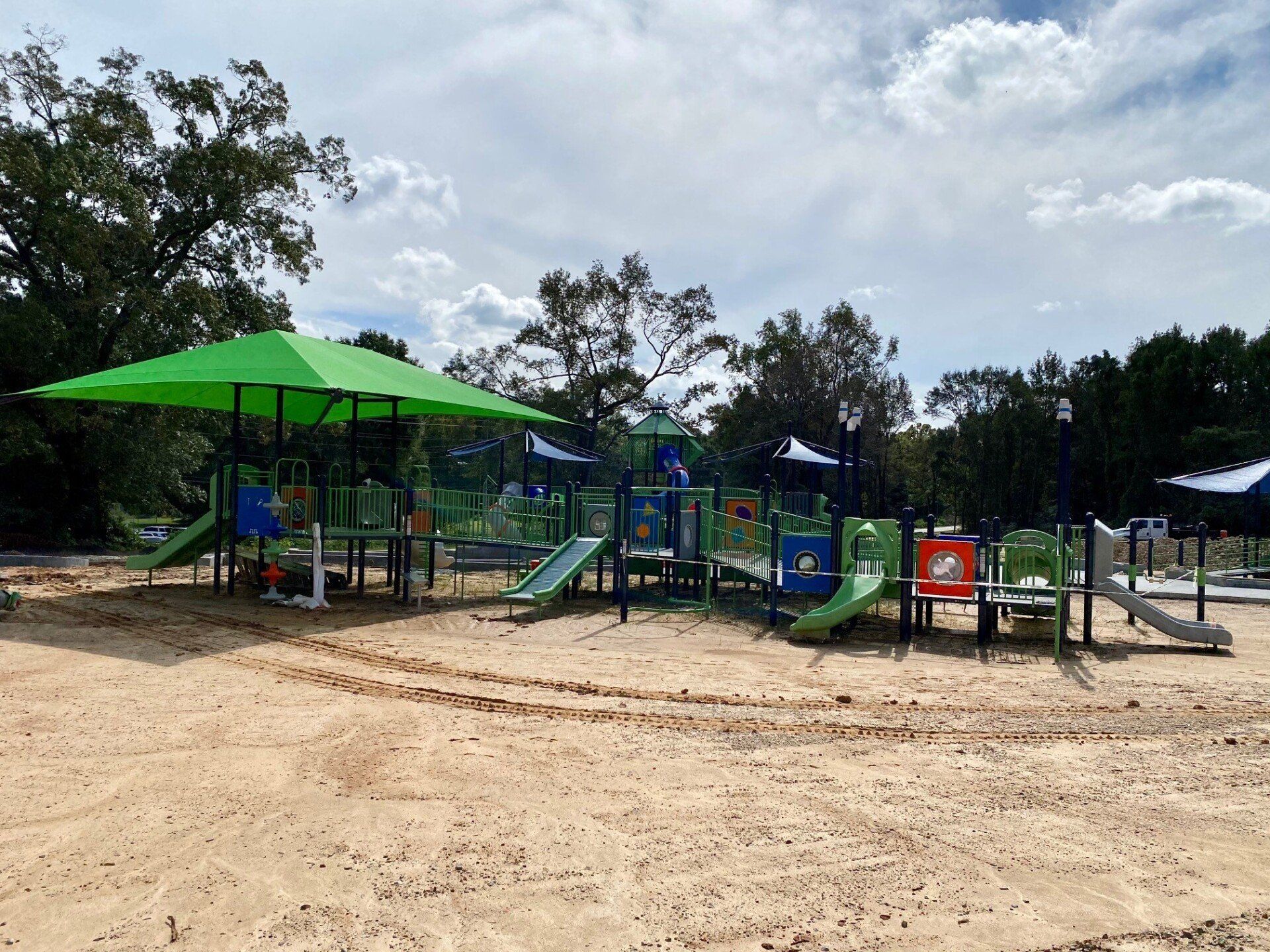 A playground with a green umbrella in the middle of it.