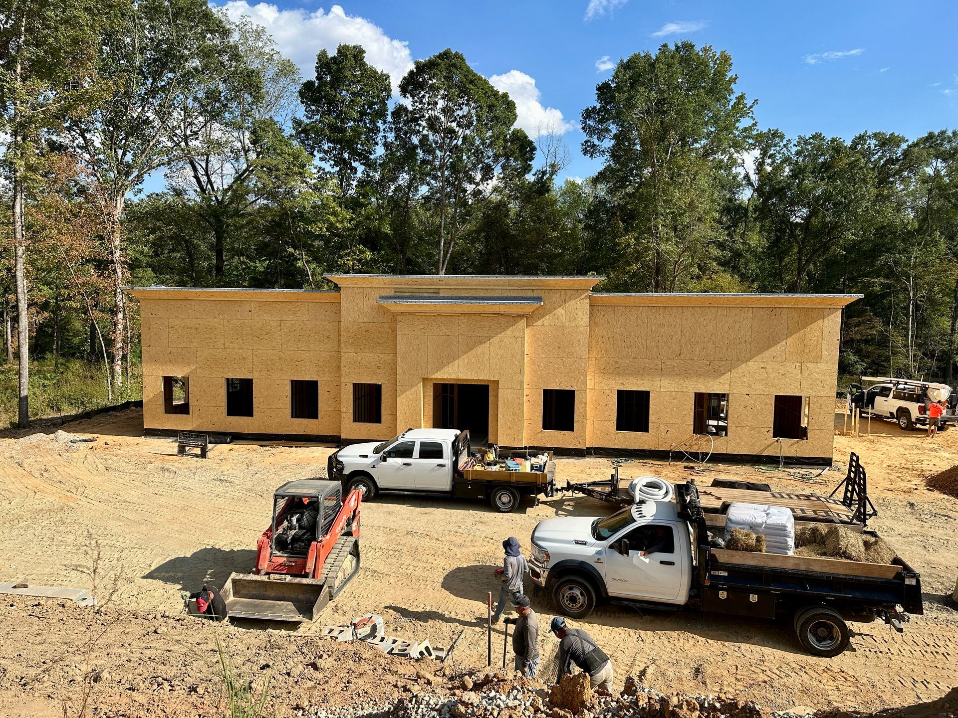 Construction site with a partially built wood-framed building, vehicles, and workers.