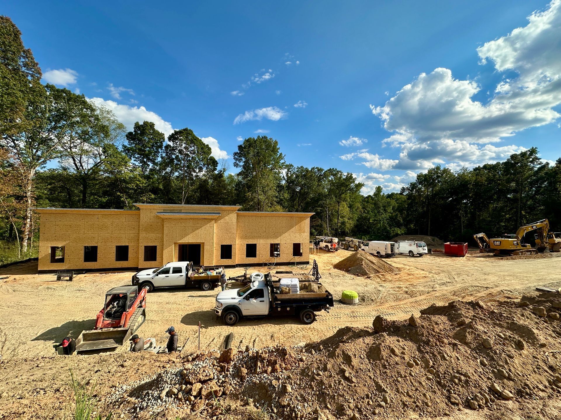 Construction site: wooden building under construction with trucks and equipment on a sunny day.