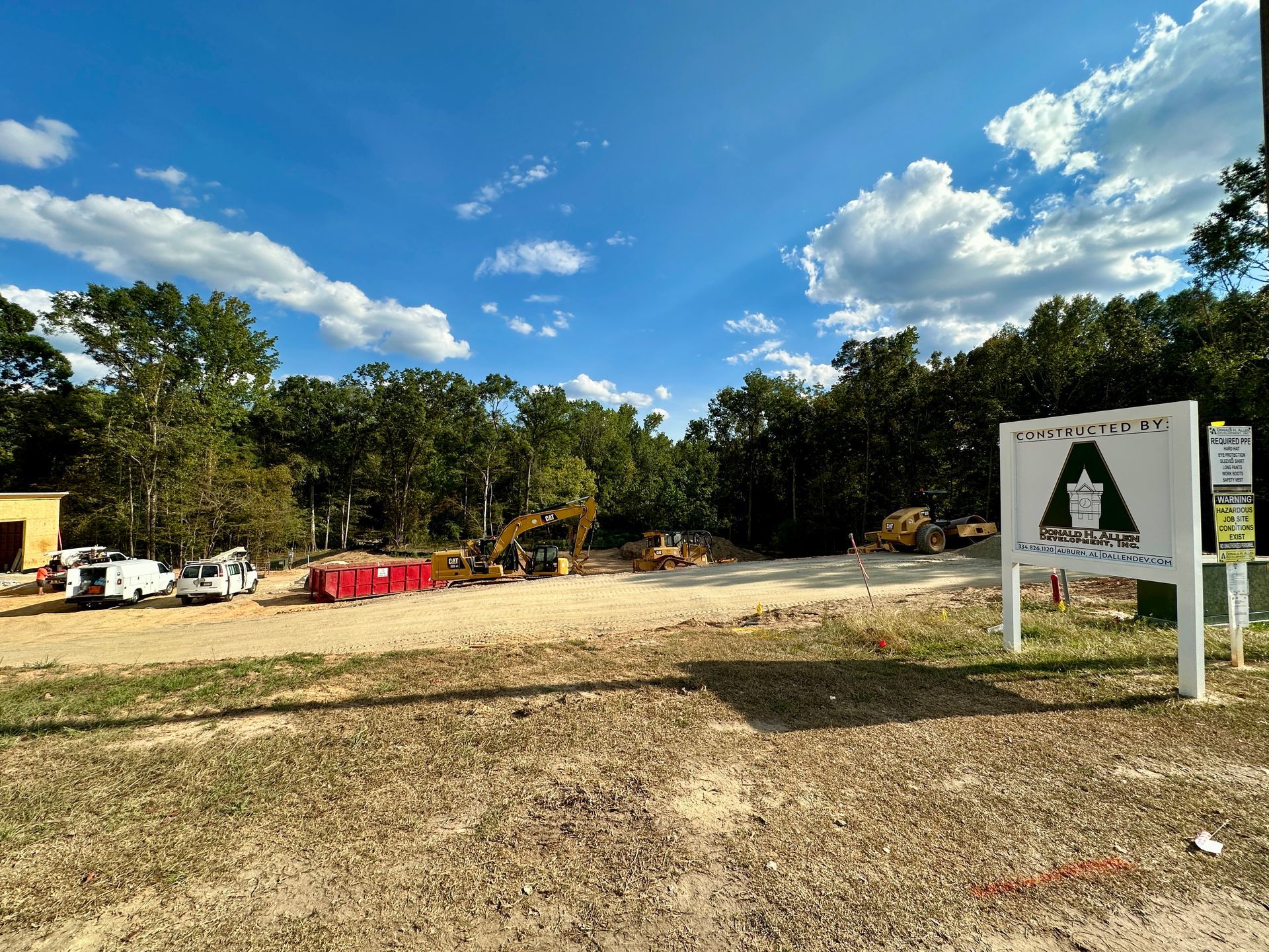 Construction site with sign, earthmovers, and vehicles under a blue sky.