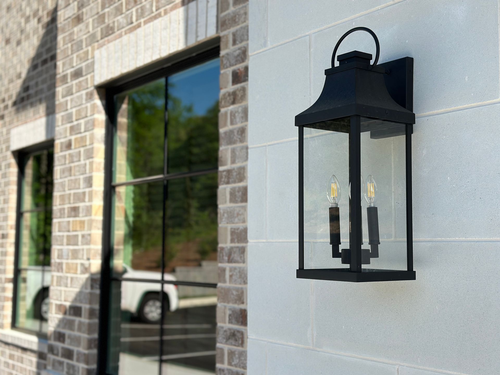 A black, rectangular outdoor lantern light fixture is mounted on a light-colored, textured stone wall next to a window.