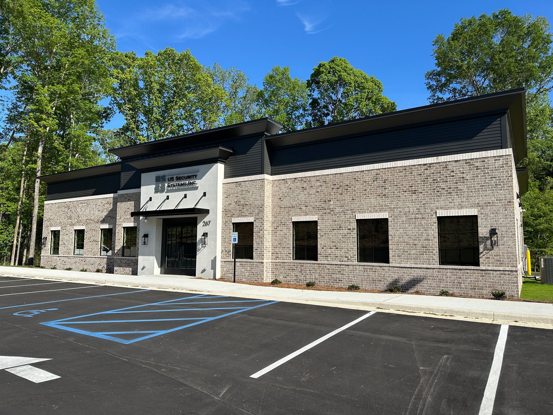 A modern, one-story brick office building with a black roof and a parking lot with marked handicap spaces. US Security Systems Inc